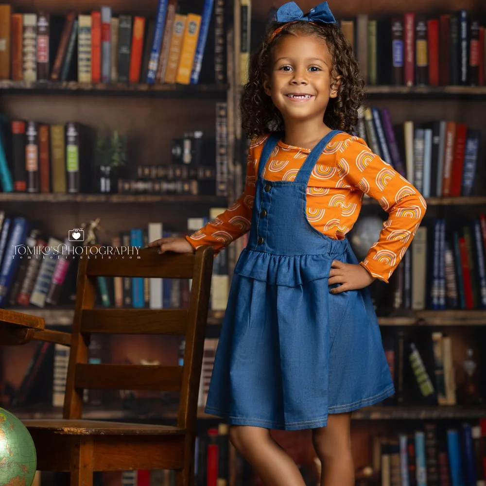 A child in a photography studio with a library shelf background, capturing a back-to-school themed photo in Birmingham, Alabama.