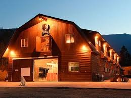 A multi-story wooden building at dusk with warm interior lighting and a mountain backdrop.