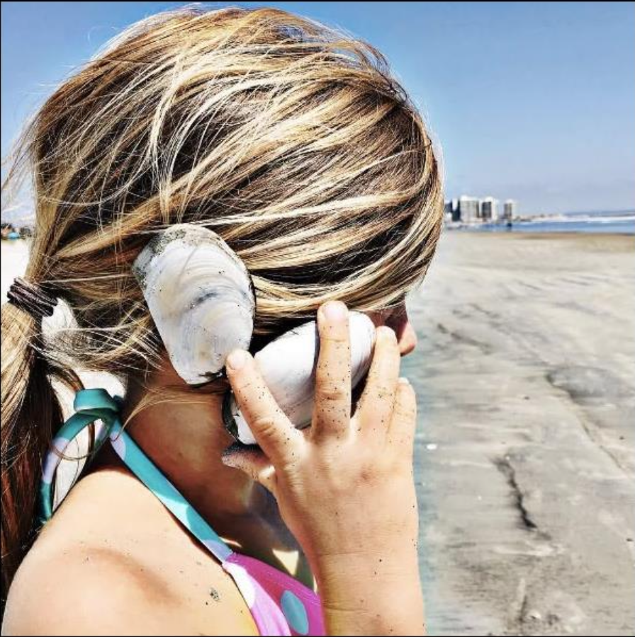 young girl holds sea shell to her ear while at the beach