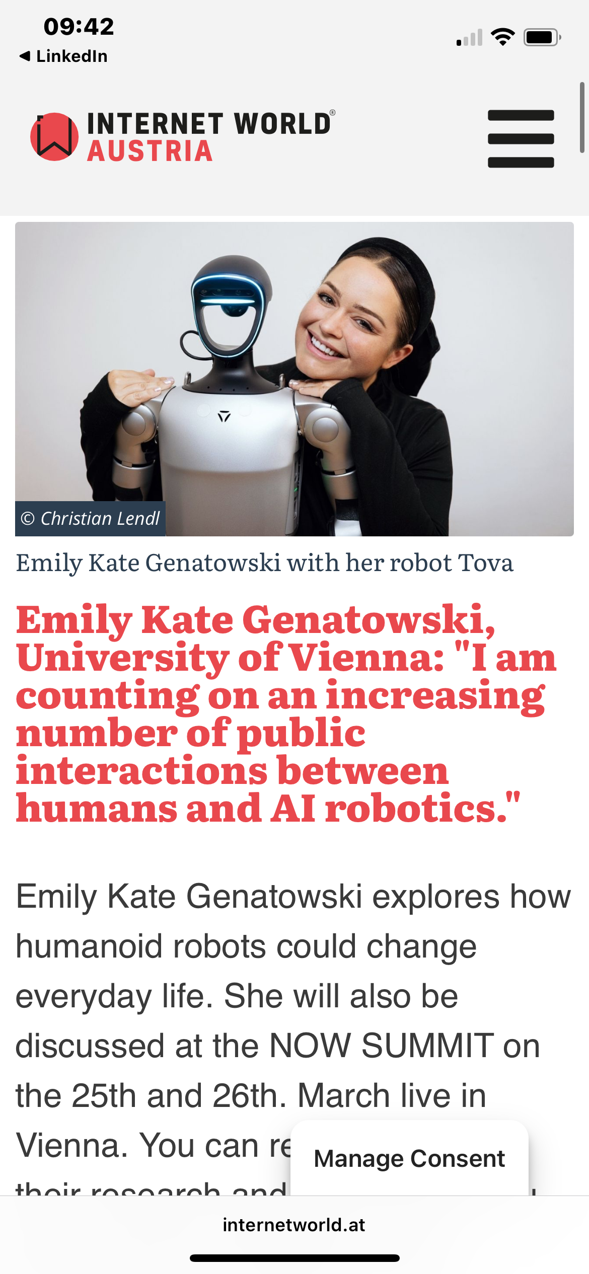 A woman on stage smiling and gesturing while standing next to a humanoid robot during a presentation or conference.