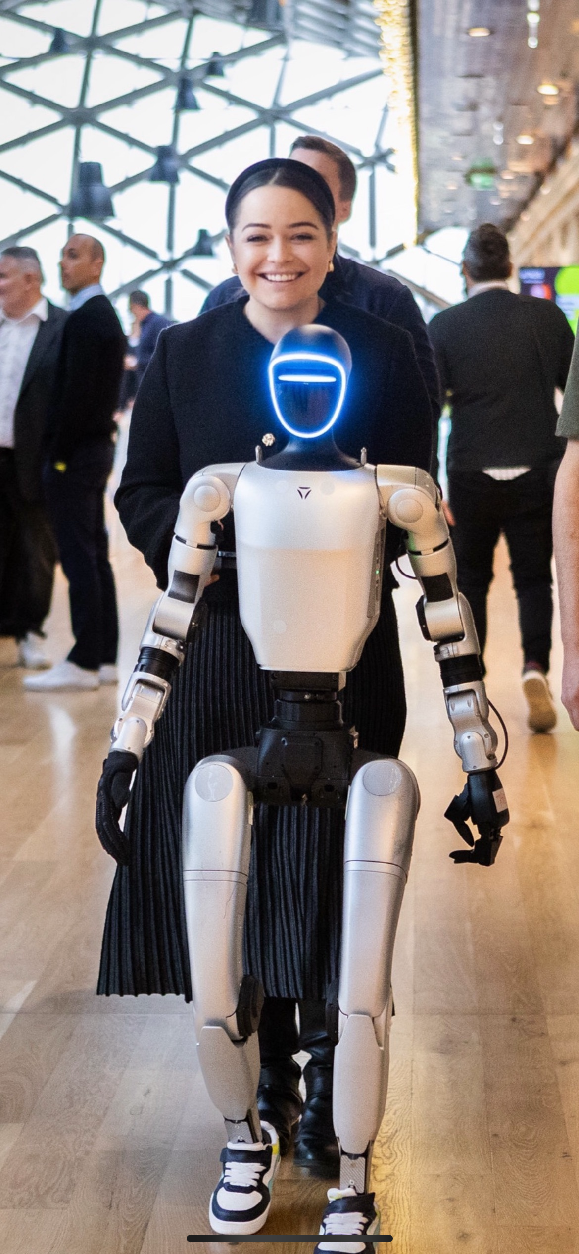 A woman giving a presentation to a humanoid robot in a wood-paneled room.