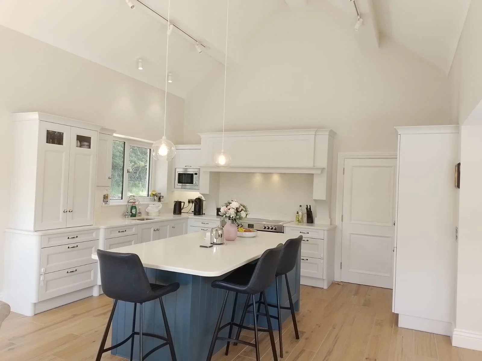 Modern kitchen with white cabinets, a central island with bar stools, pendant lighting, and light wood flooring.