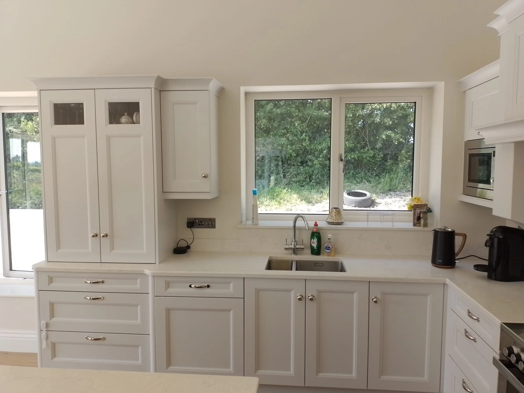 Kitchen with white cabinets, a countertop, a sink, a window view of greenery, and kitchen appliances including a kettle and coffee maker.