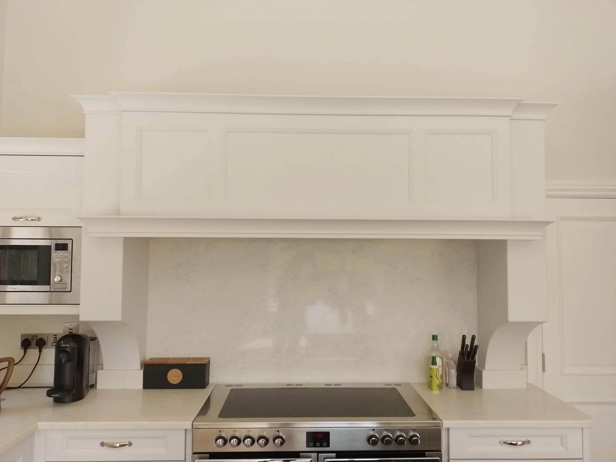 Modern kitchen with white cabinetry, integrated microwave, espresso machine, electric stovetop, and marble-like backsplash.