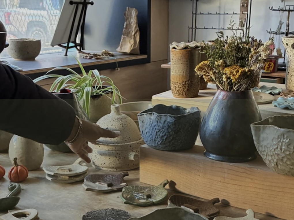 An arm reaches for a piece of hand-made pottery on a table full of hand-made pottery pieces.