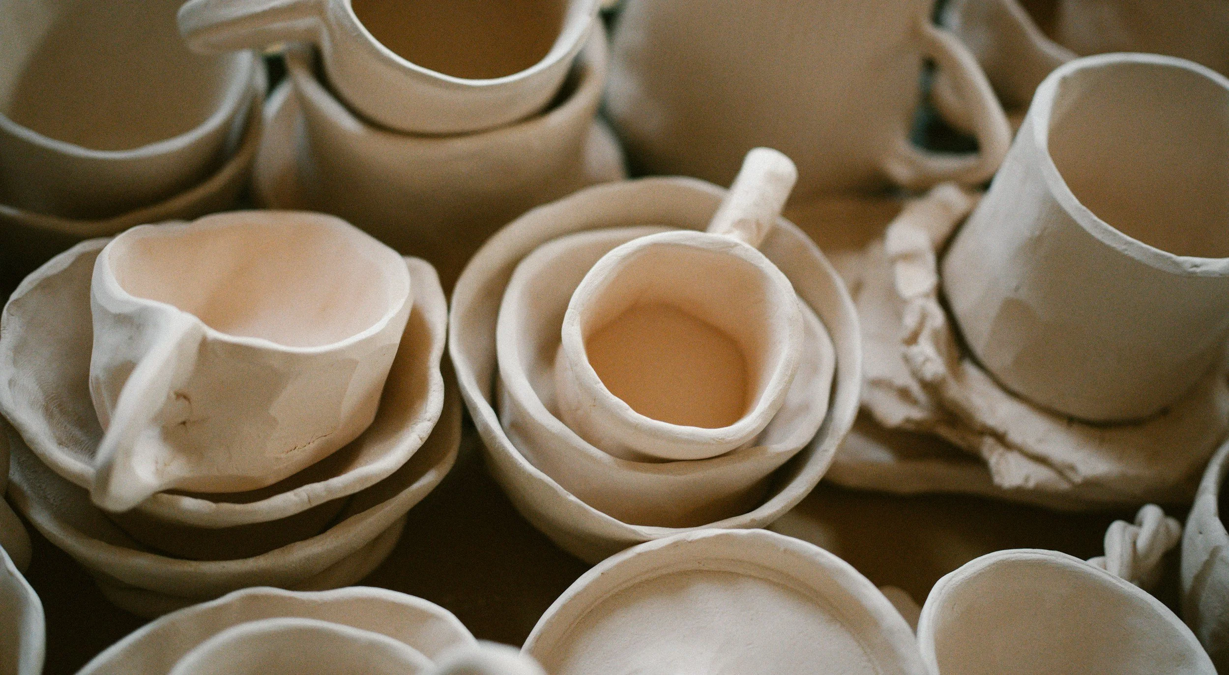 A table top is covered with stacks of handmade, ceramic cups and bowls awaiting glaze.