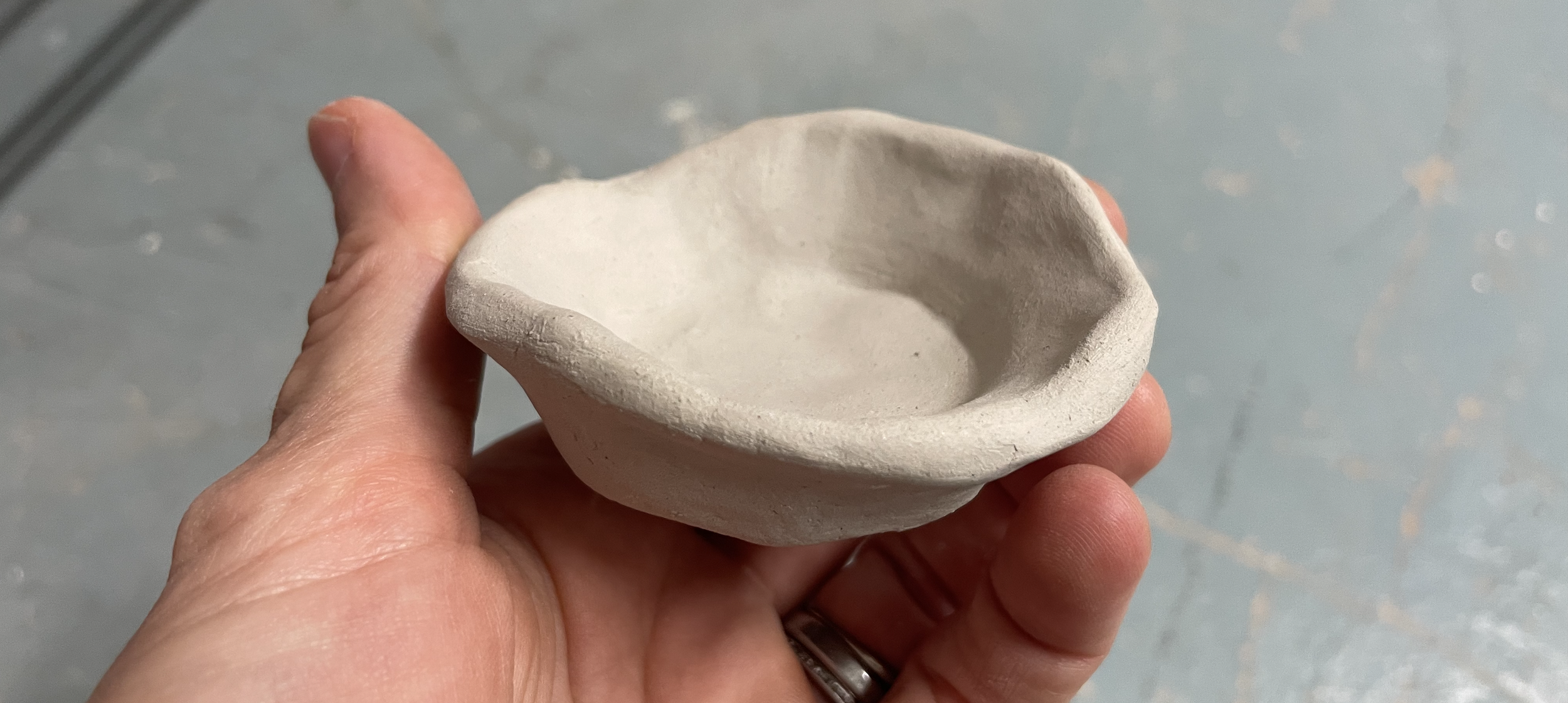A hand holds a small hand made bowl.