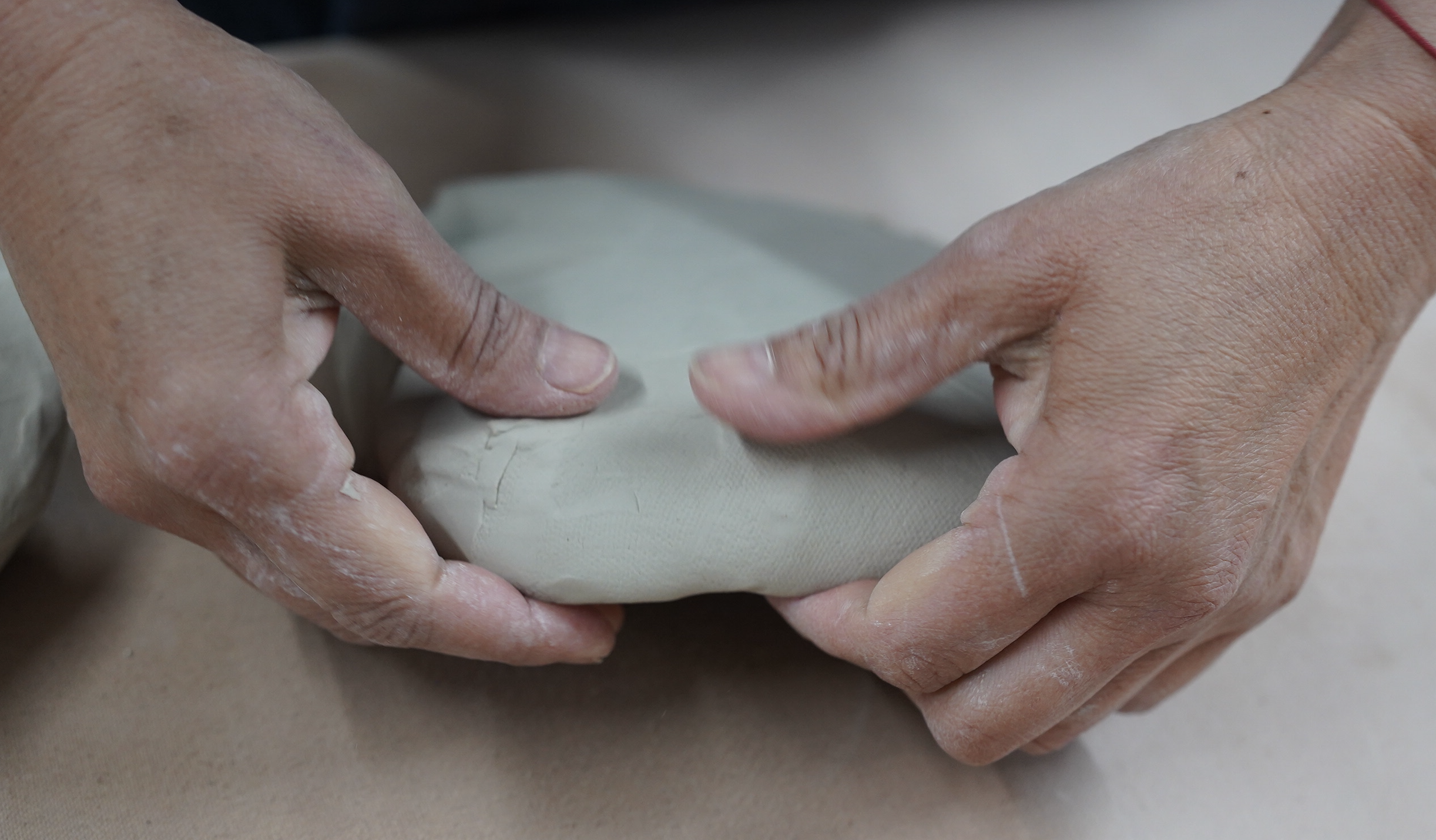 Two hands shape a ball of clay into a flat disk.