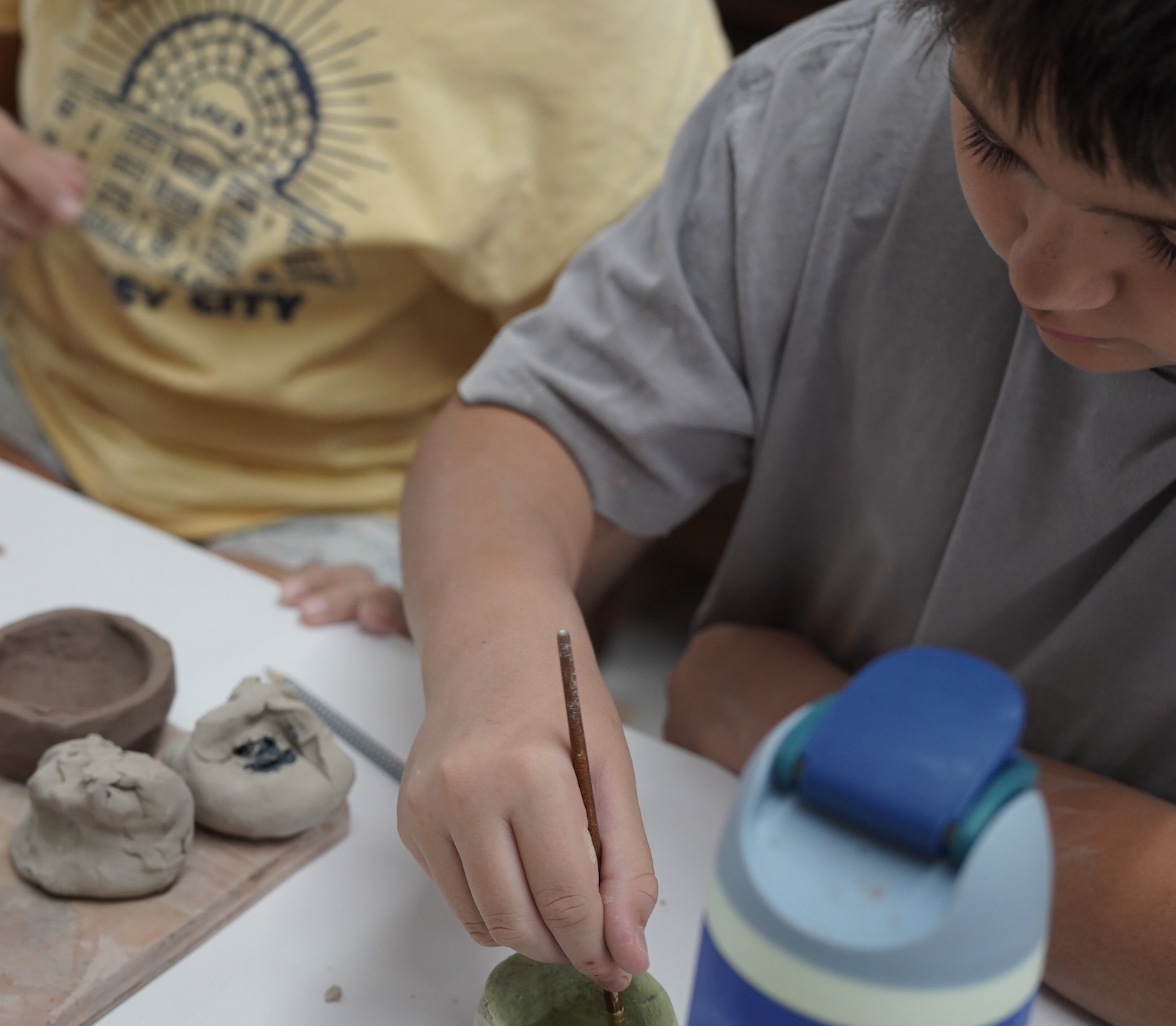 A teenager paints a homemade ceramic bowl.