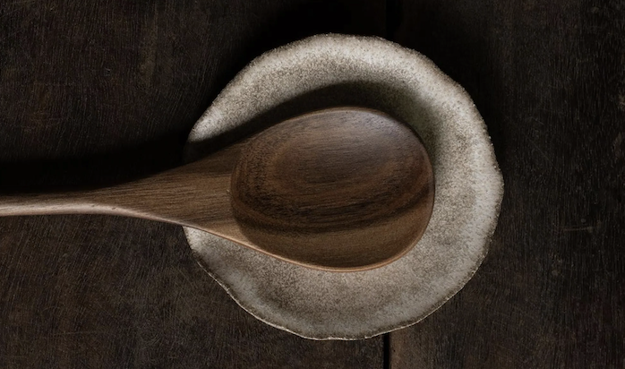 A wooden spoon rests in a charming handmade ceramis spoon rest.