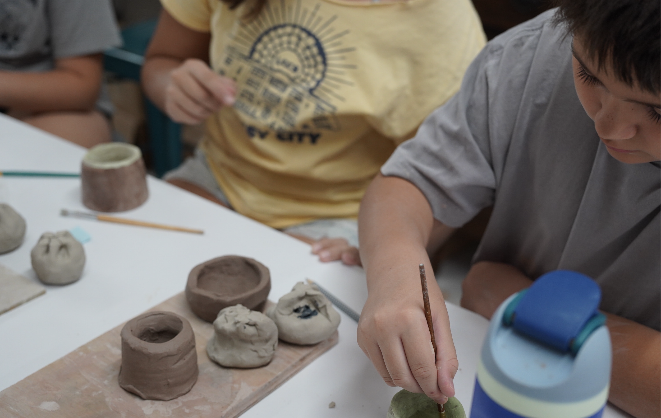 Two teens paint hand made pottery pieces at a shared table.