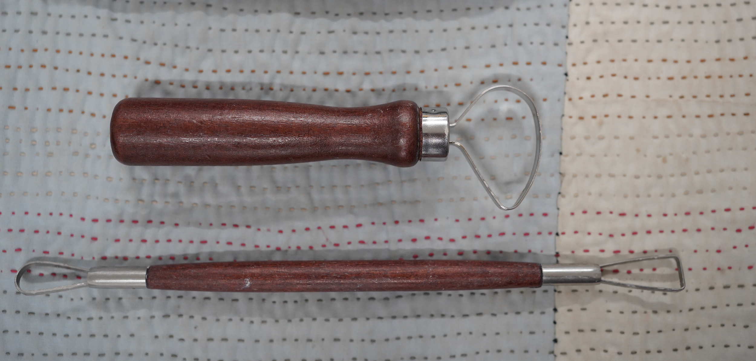 Two loop tools for trimming pottery with wooden handles lay next to each other..