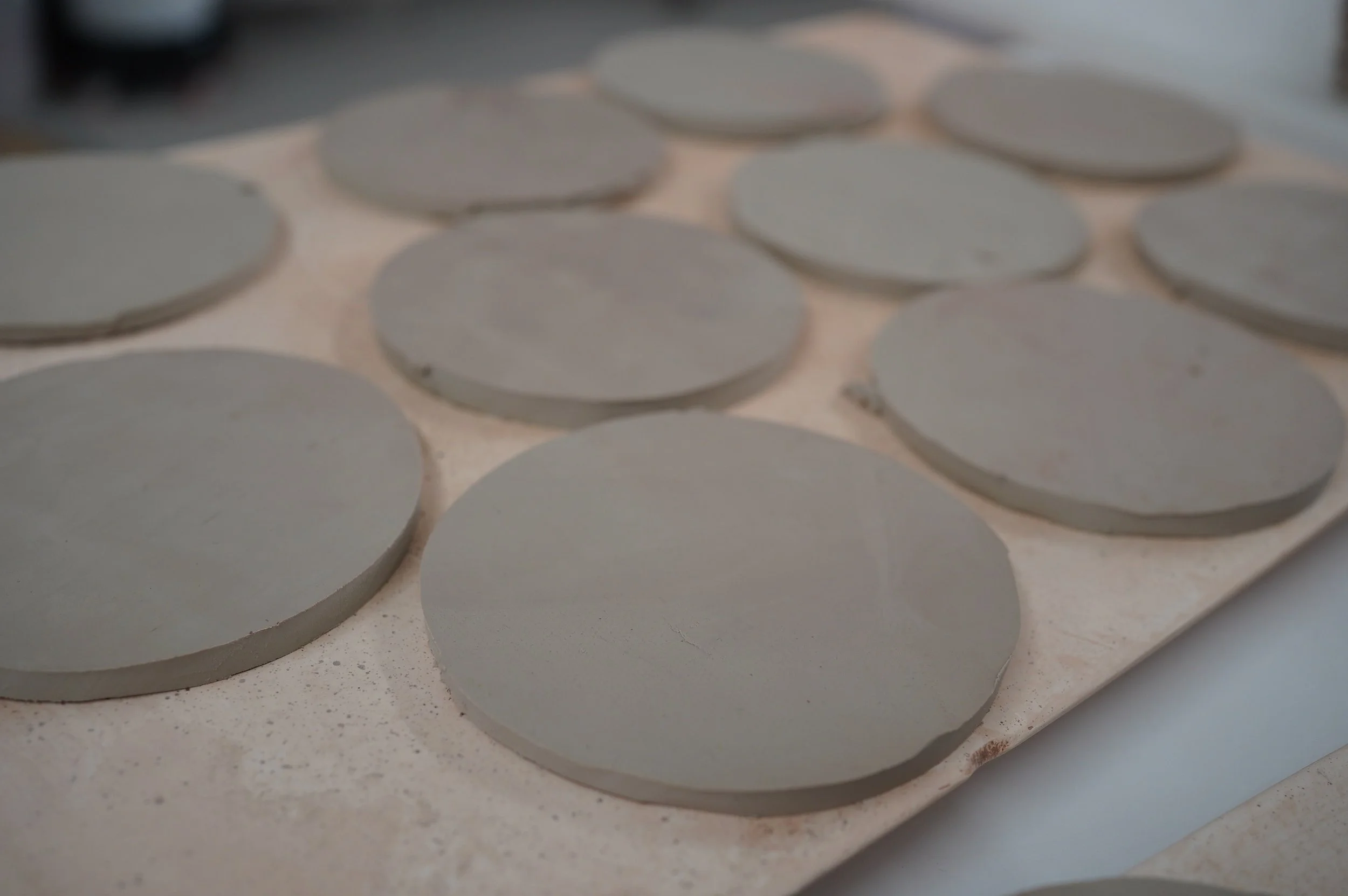 Many leather hard clay coasters are lined up on a board to dry.