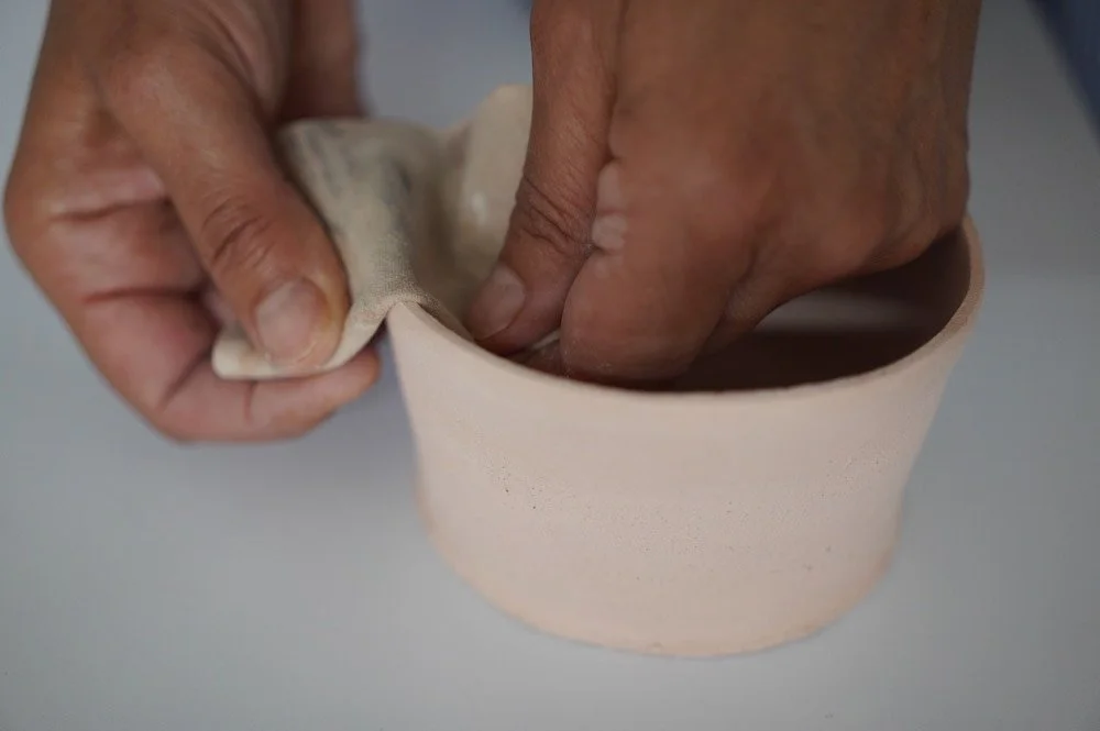 Two hands use a chamois to smooth the rim of a bowl.