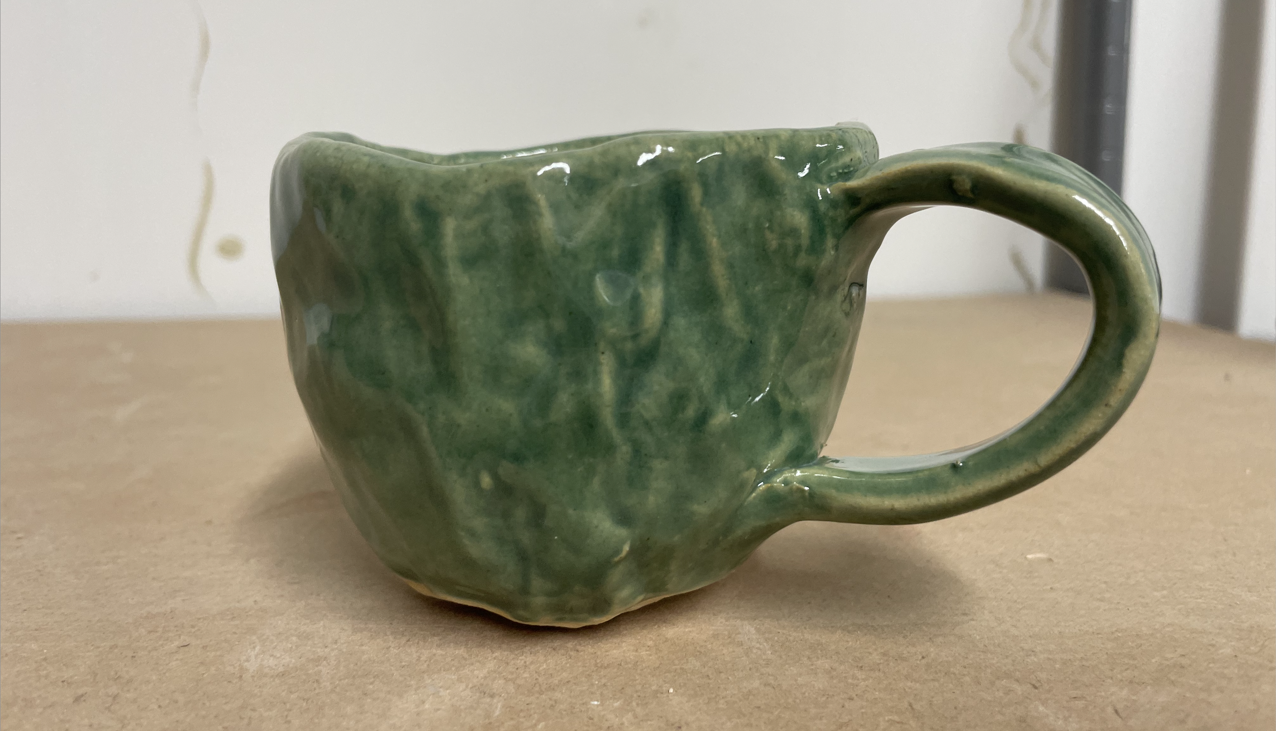 A roughly shaped handmade mug sits atop a shelf.