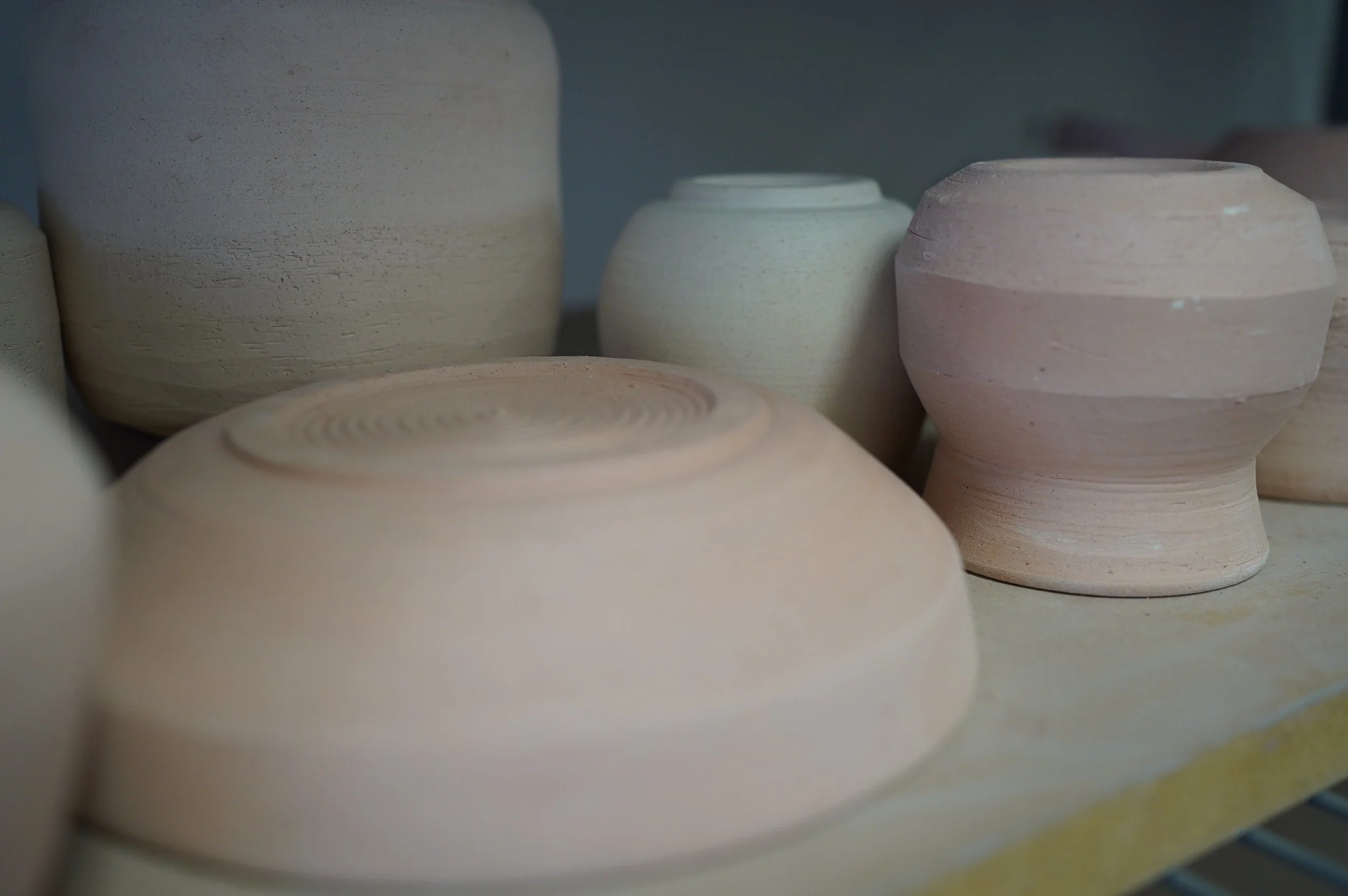 Bisque pots are lined up on a shelf.
