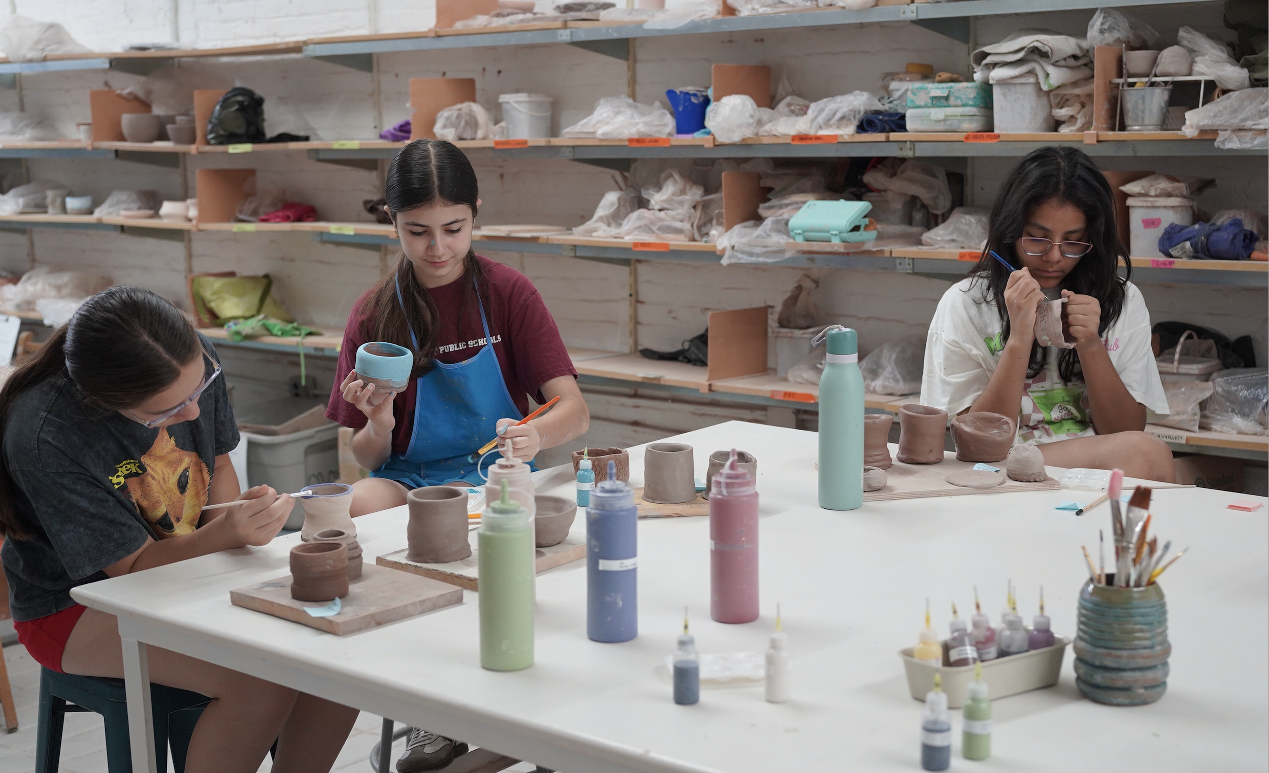 Three teenage girls paint their pottery projects around a large table in Atacama Ceramics Studio.