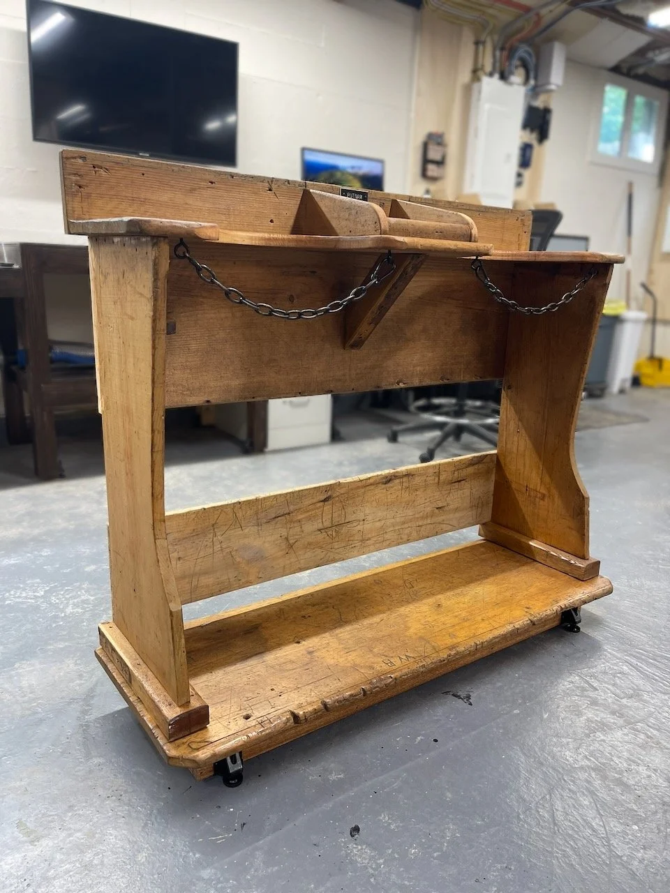 Old wooden rolling cart with chains hanging from the top shelf in a workshop or garage.
