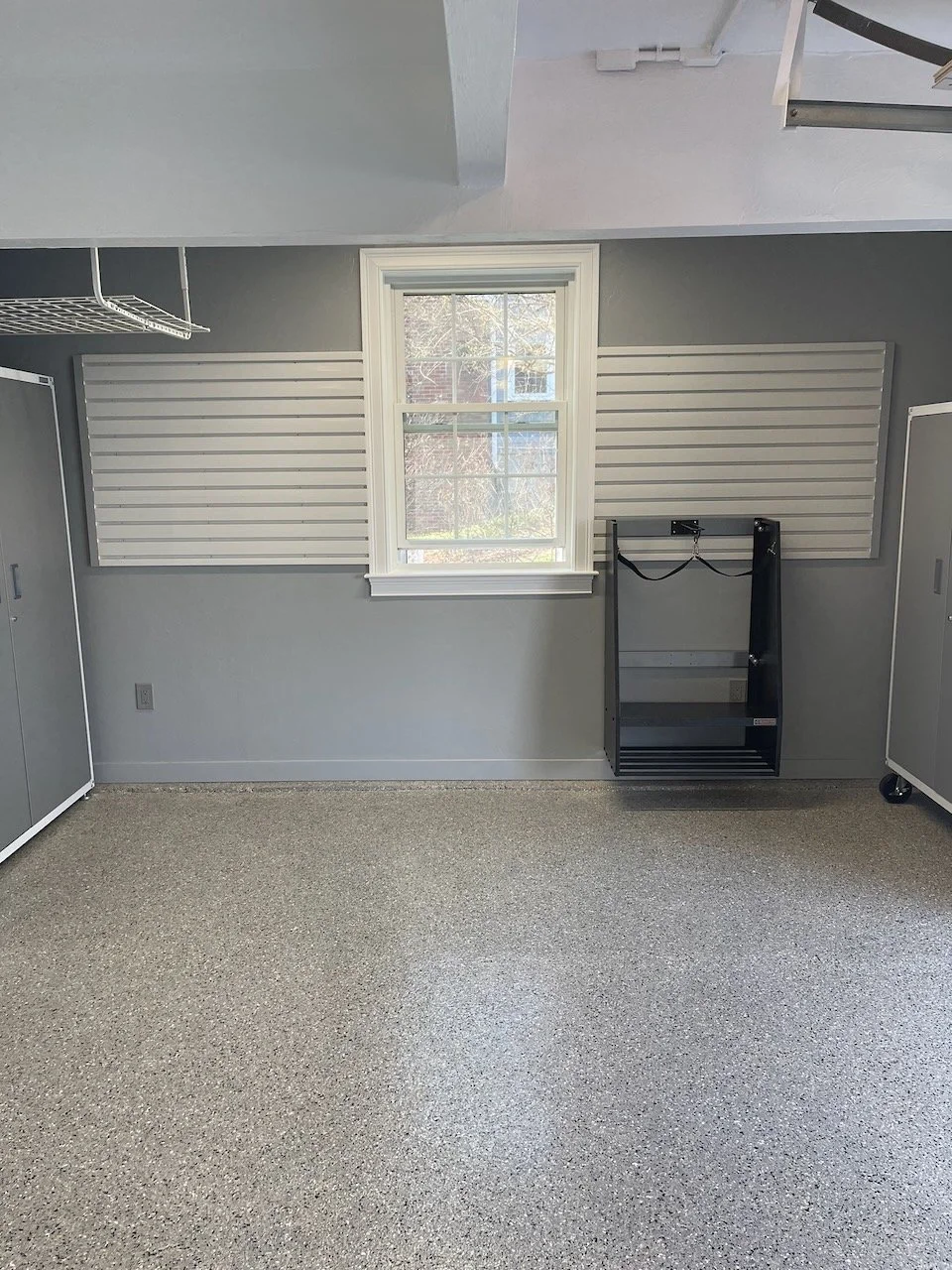 Empty garage or storage room with a window, gray walls, and pegboard panels on the wall.