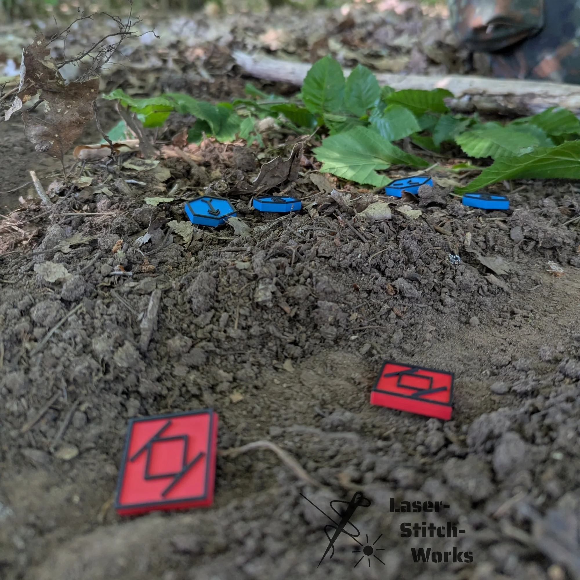 Auf dem Boden liegende Spielkarten in Rot und Blau sowie ein Logo mit der Aufschrift "Laser-Stitch-Works" im unteren rechten Bildbereich.