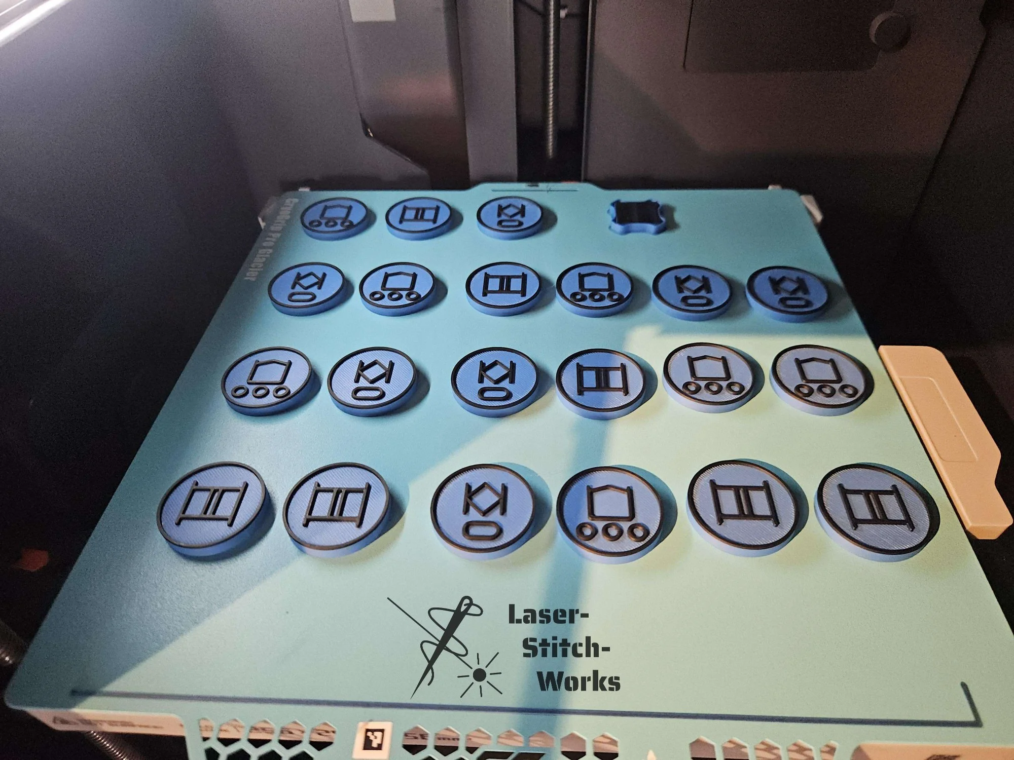 Kleines Handarbeitsgerät mit runden Kunststoffplatten, die verschiedene Nadel-Designs für Laser-Stickarbeiten zeigen. Das Gerät ist bläulich und hat die Beschriftung "Laser-Stitch-Works".