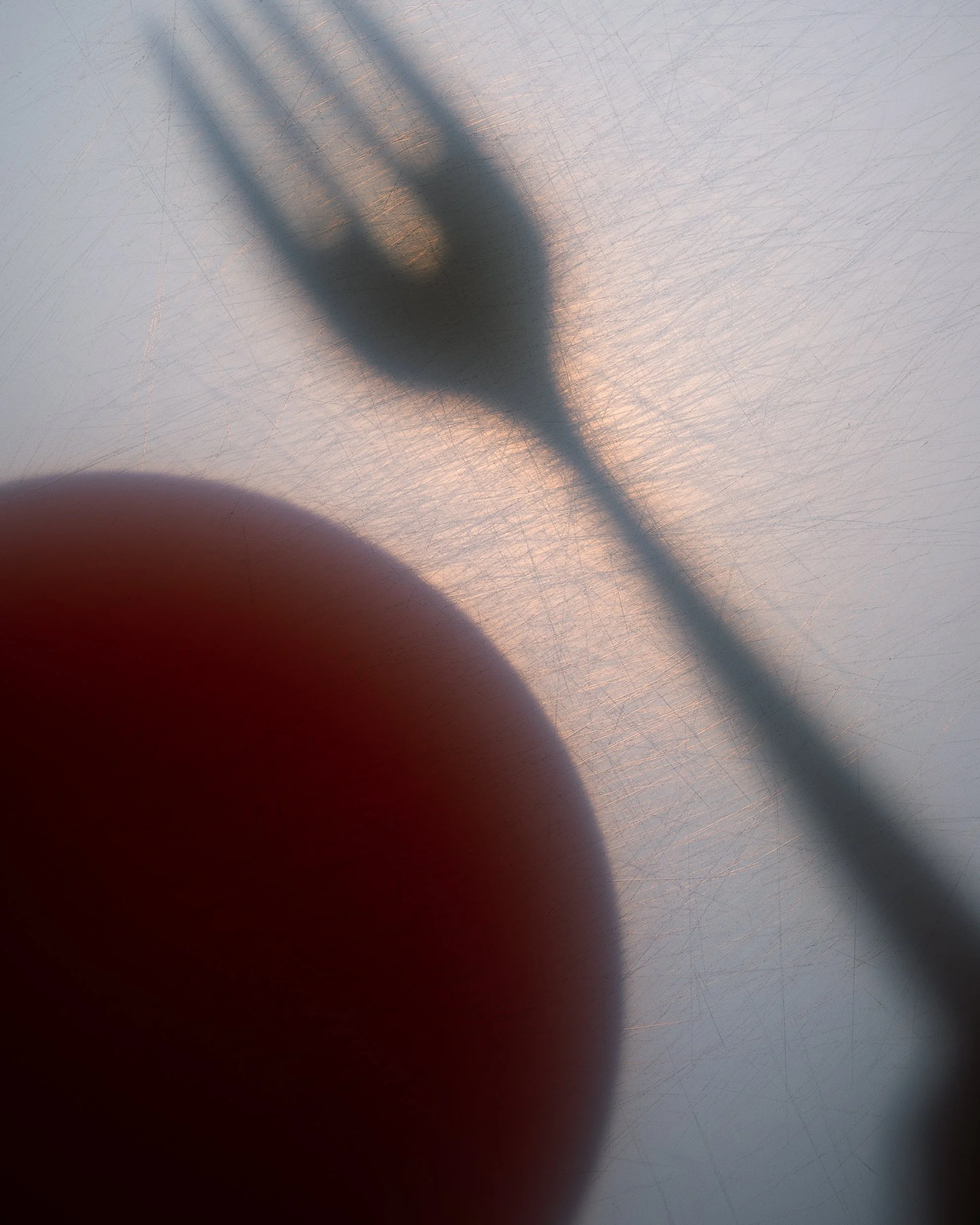  A blurred shadow of a fork and a round red object on a scratched, translucent surface with soft lighting. 