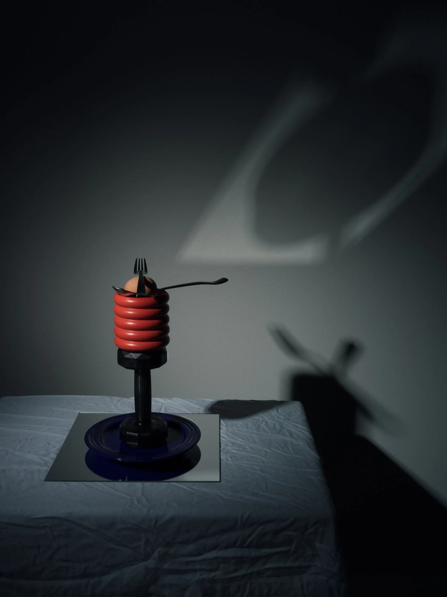  A fork, spoon, and egg sit on top of an orange vase atop a black dumbbell, blue plate and a square mirror, sitting on a covered table with dramatic shadows and lighting creating abstract shapes on the wall. 