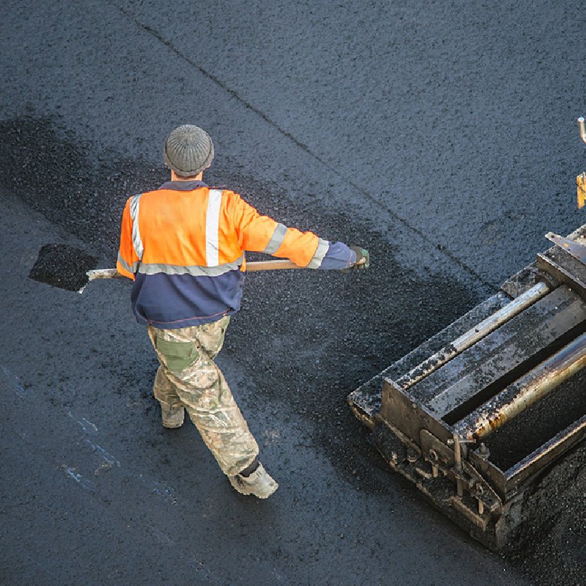 Construction man with shovel of asphalt helping lay out asphalt.