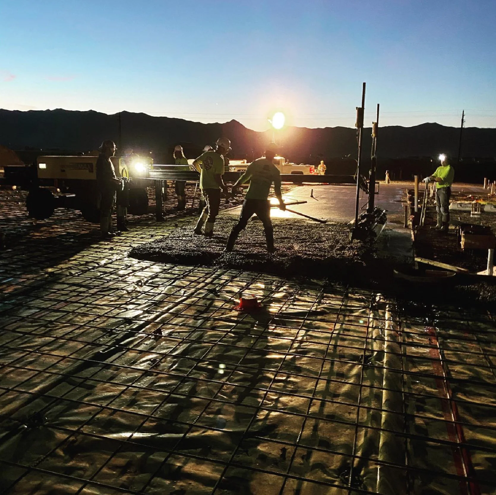 Construction workers laying concrete at dusk.