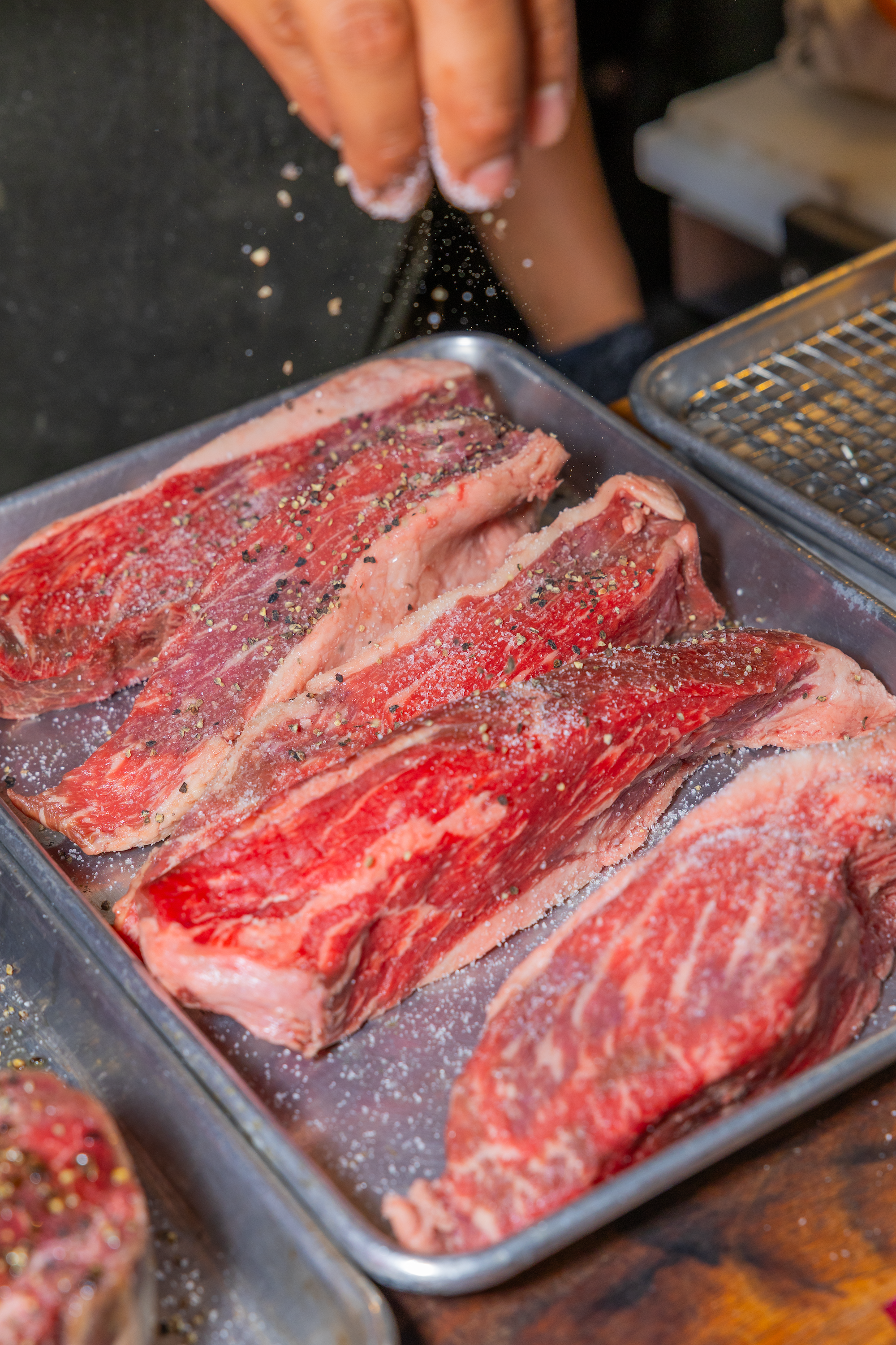 Raw beef ribs seasoned with salt, pepper, and herbs in a metal tray, being prepared for cooking.