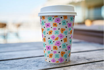 Colorful floral-patterned paper coffee cup on wooden table outdoors.