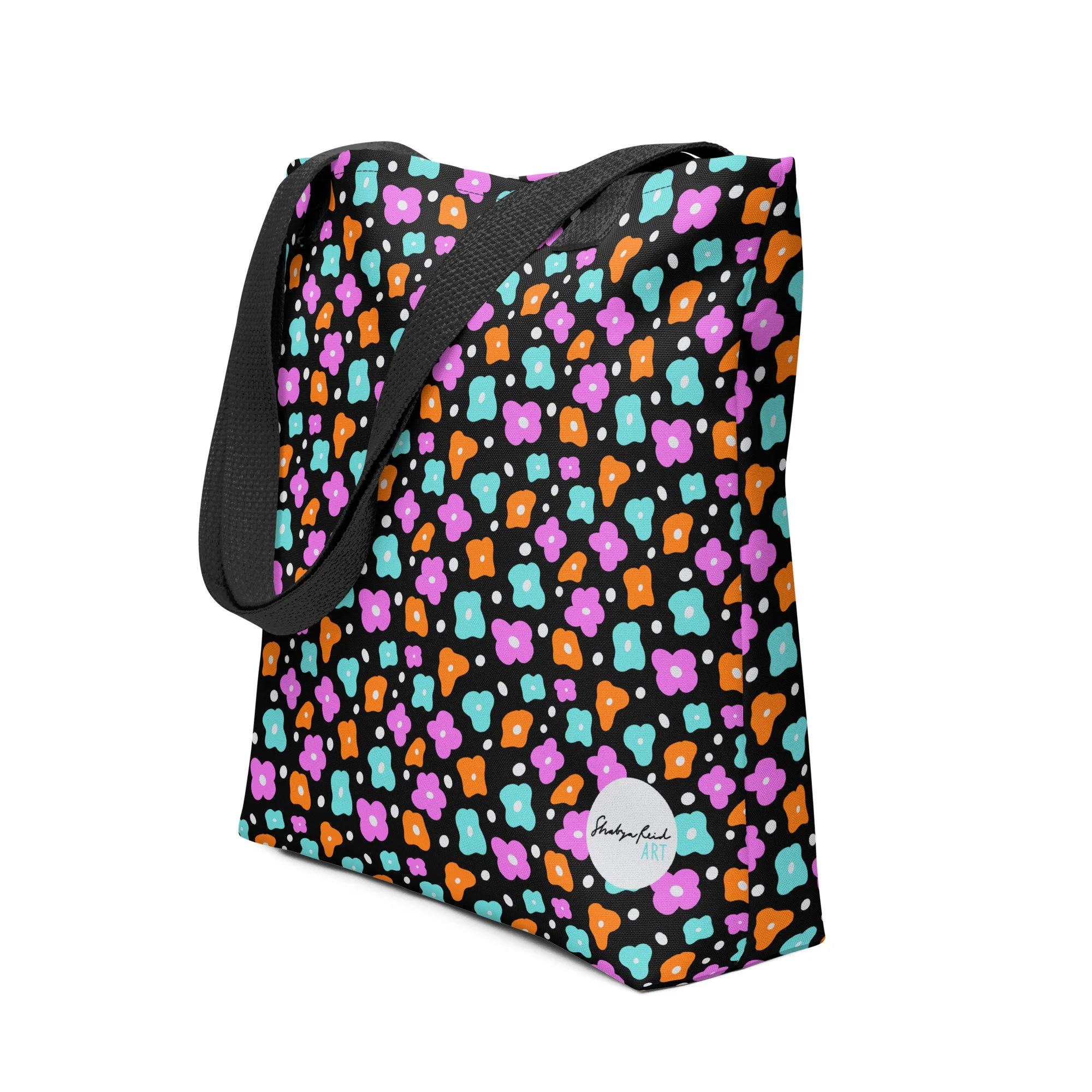 Colorful floral-patterned tote bag with black straps, featuring a design of pink, turquoise, and orange flowers on a black background. Includes a circular logo reading 'Shaayghedi Art.'