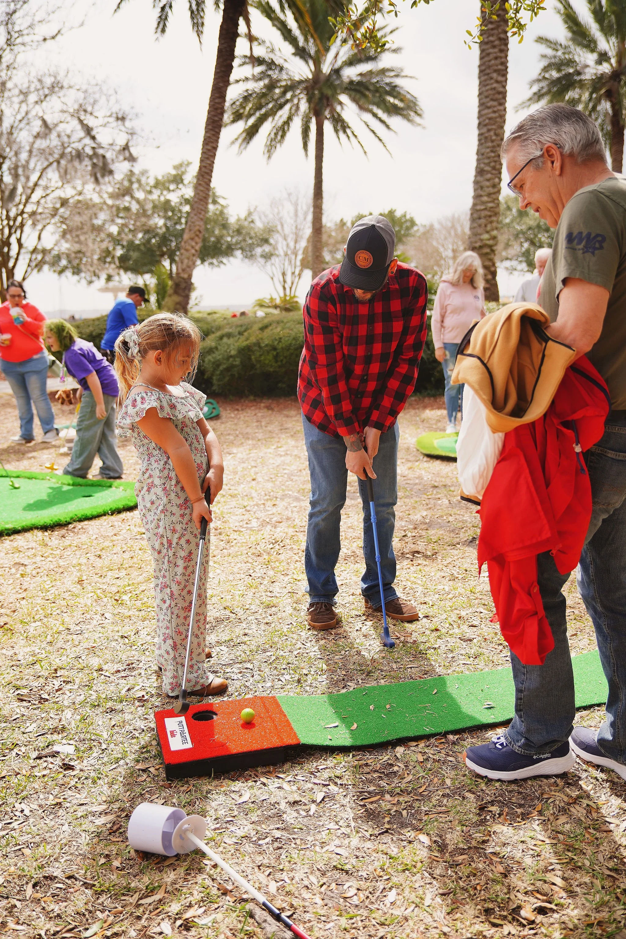 People playing mini golf outdoors among palm trees