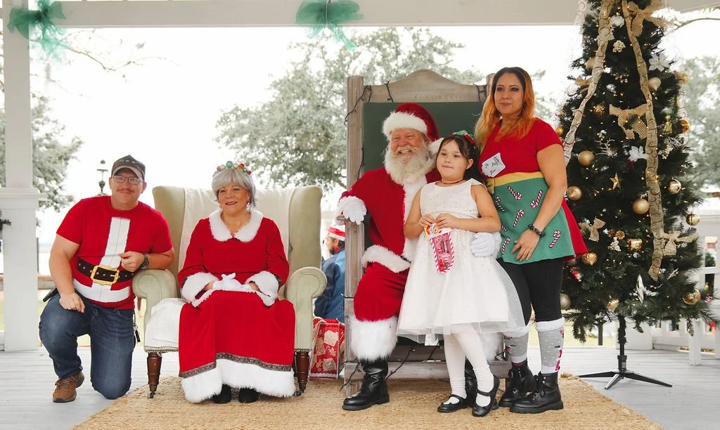 People celebrating Christmas with Santa Claus, a woman, and a girl in front of a decorated Christmas tree.
