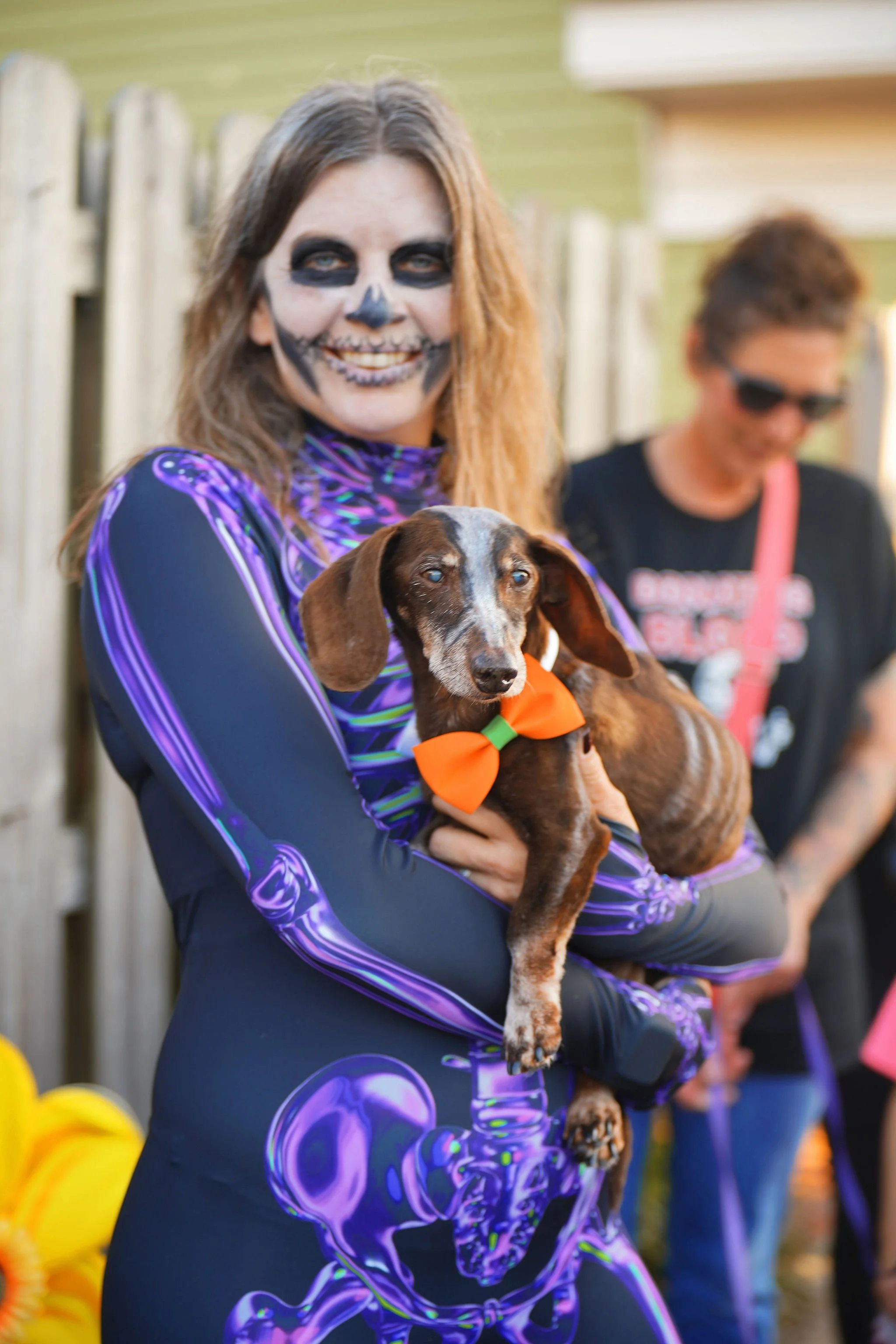 Woman dressed in skeleton face paint holding a Dachshund dog with a bow tie