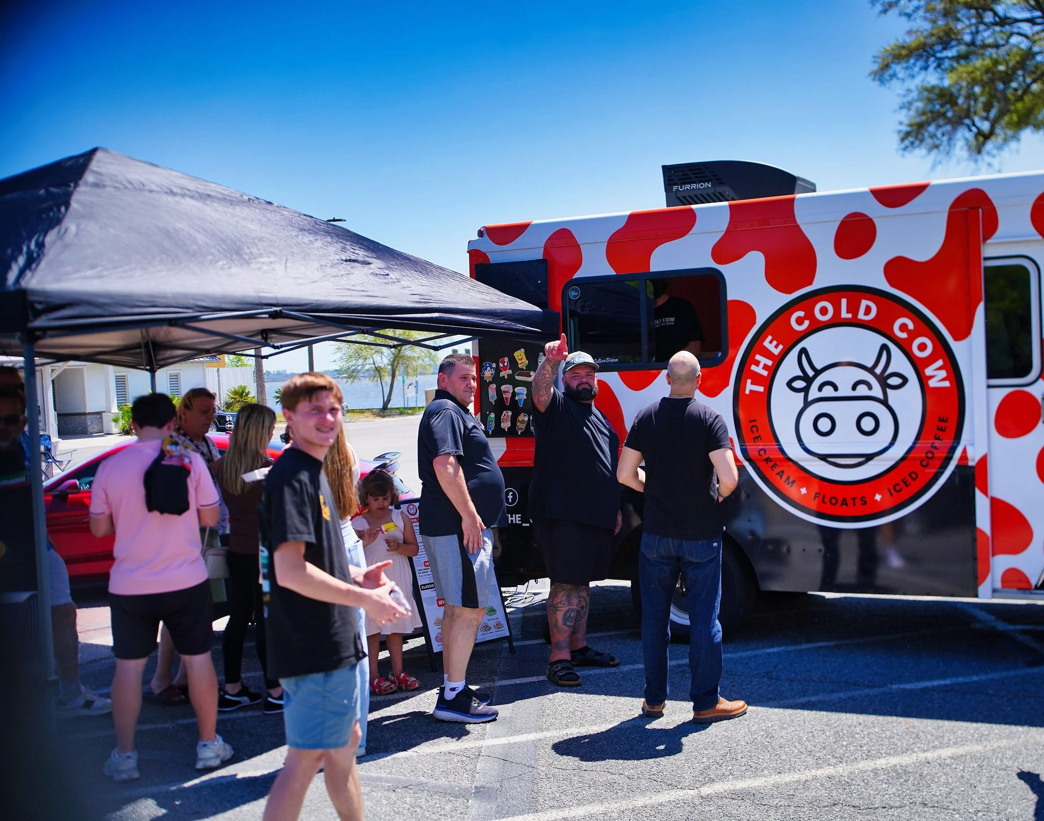 People standing outside a food truck called The Cold Cow, serving ice cream, floats, and iced coffee on a sunny day.