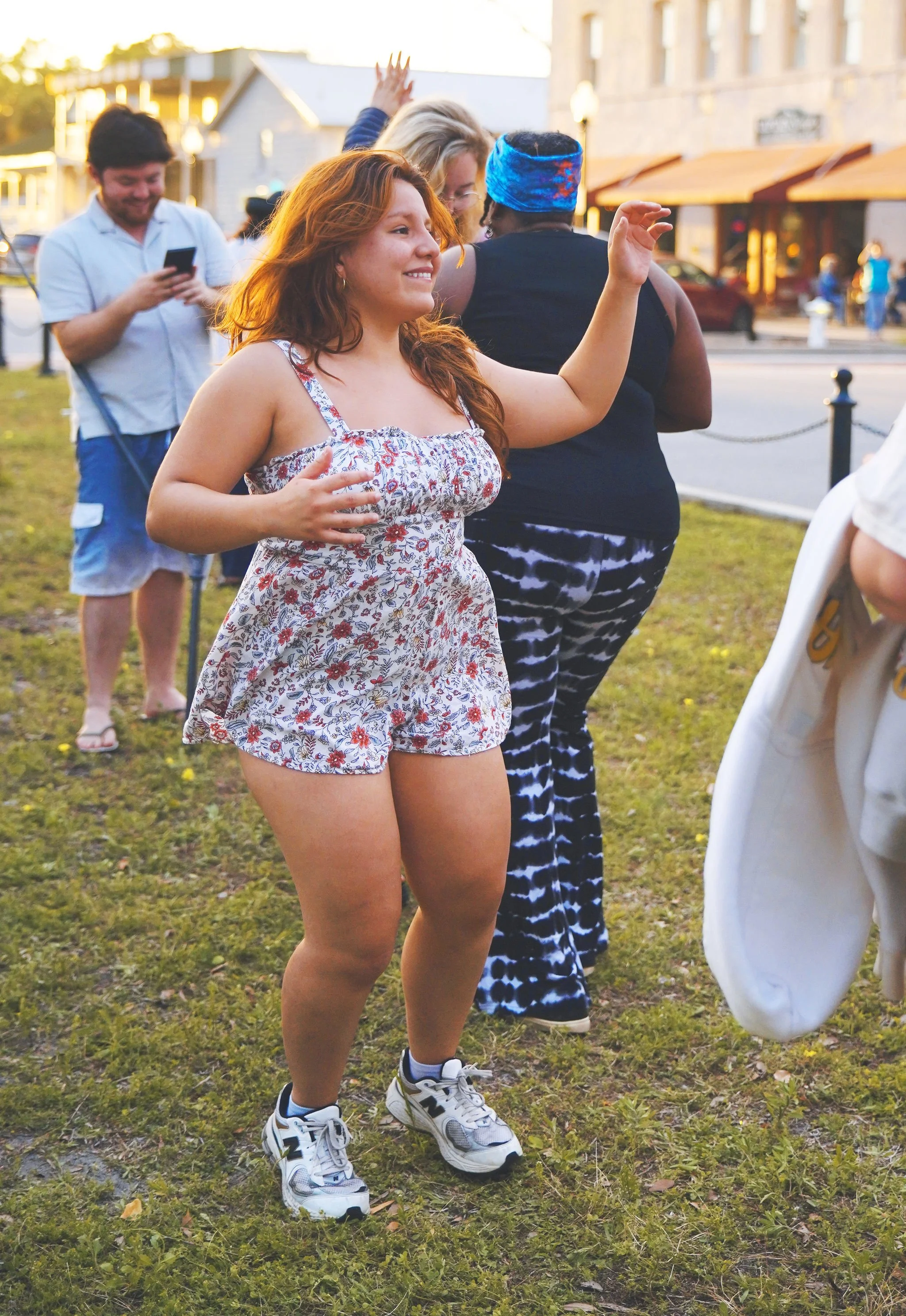 A group of people dancing and socializing outdoors on a grass area in the evening.