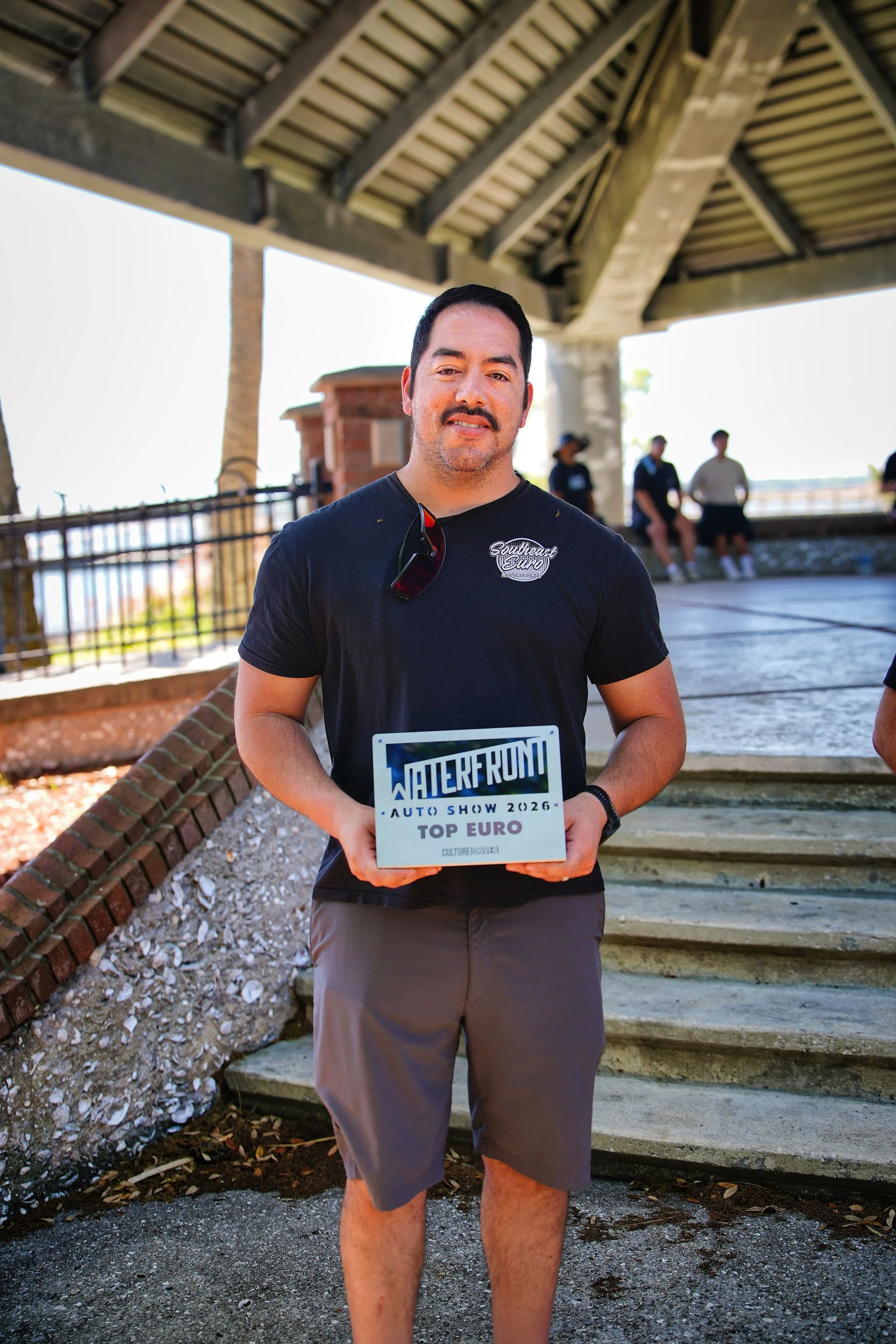 Man holding a sign that reads 'Waterfowl Auto Show 2026 Top Euro' at an outdoor event.