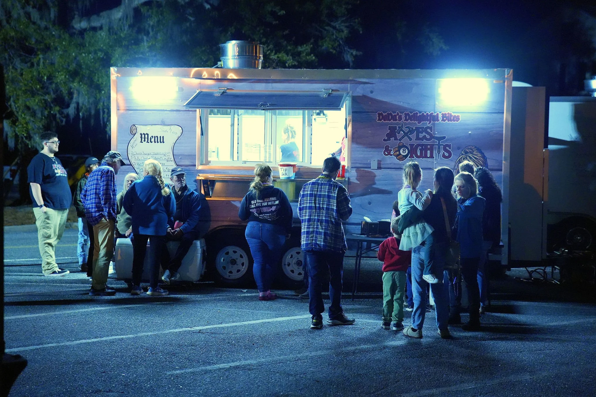 People standing in line at a food truck at night, serving baked goods and snacks.