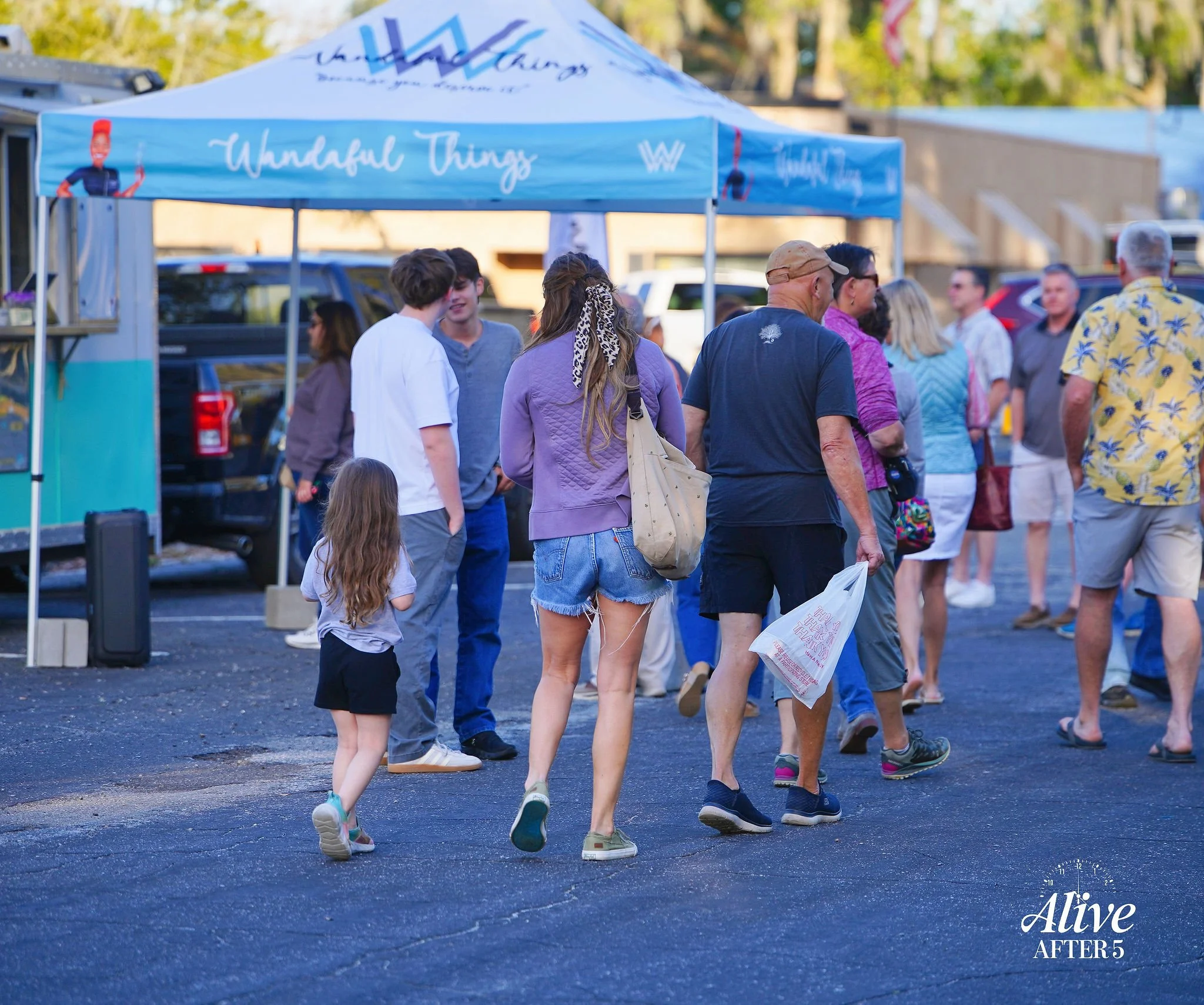 People walking in a parking lot near a tent that reads 'Wonderful Things' at an outdoor event during daytime.