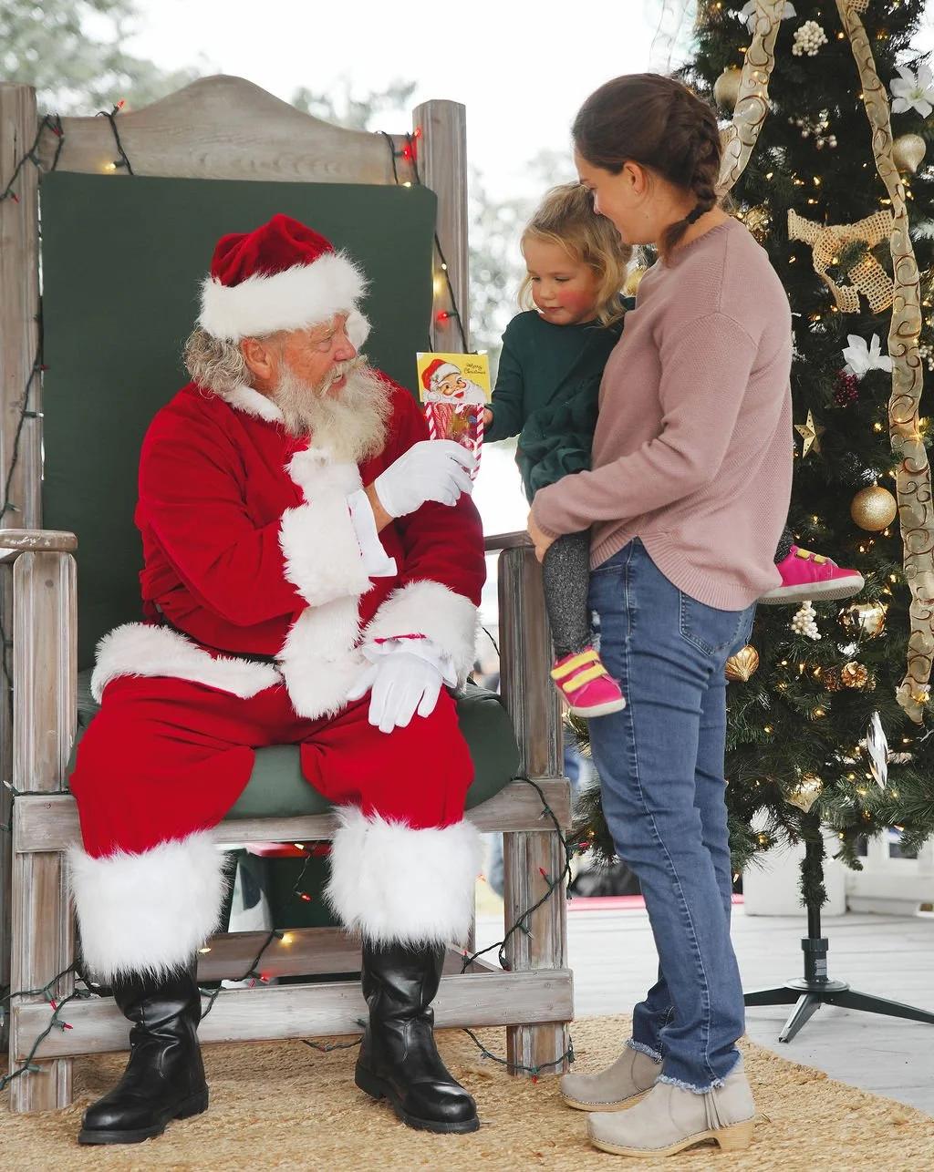 A young girl and woman talking to Santa Claus during Christmas, with a decorated Christmas tree in the background.