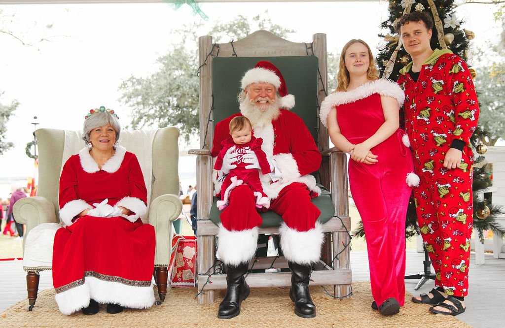 Family dressed in Christmas pajamas and outfits taking a holiday photo with Santa Claus and Mrs. Claus during Christmas celebrations.