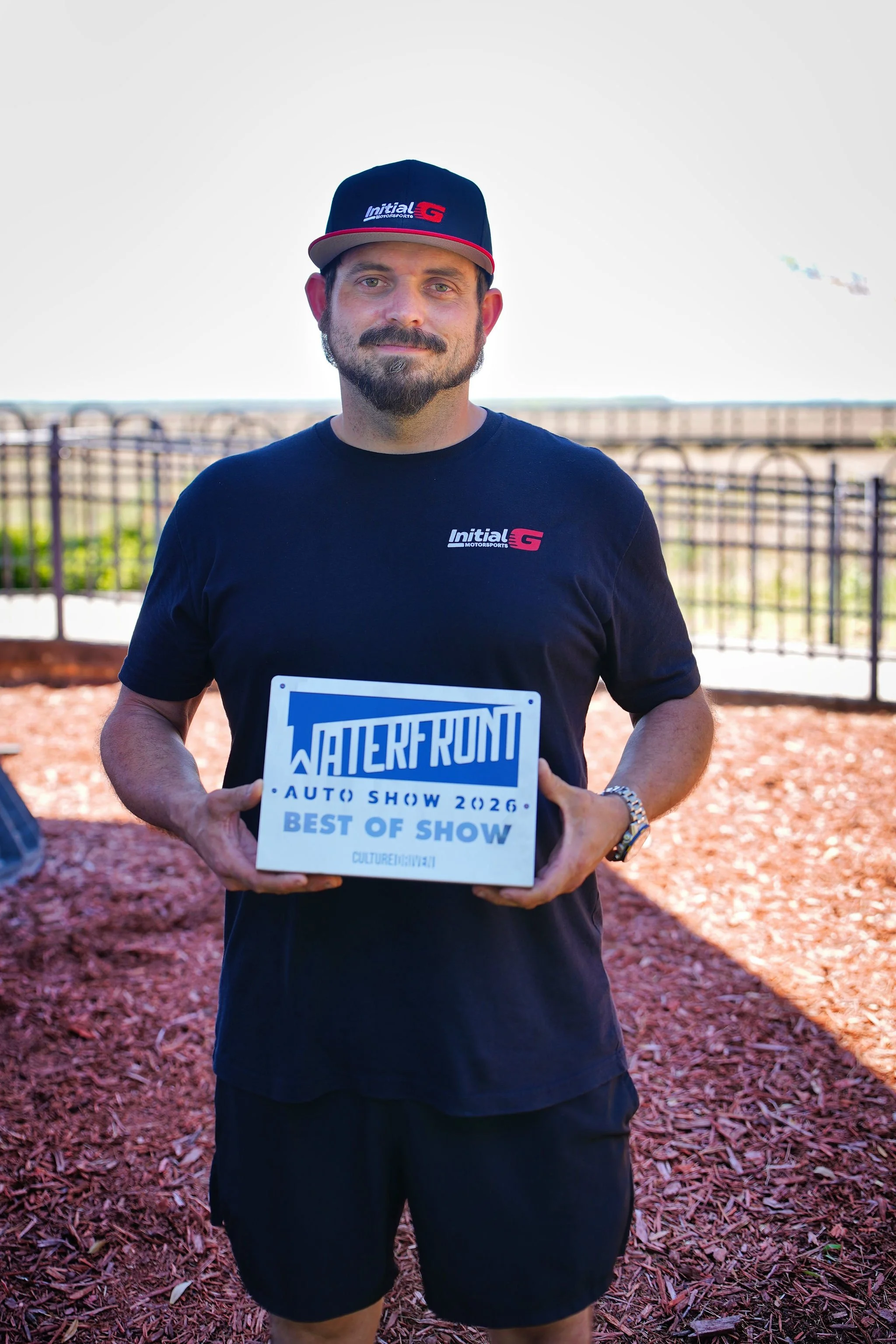 Man in black shirt and cap holding a sign that says 'Walker Run Auto Show 2026 Best of Show' at an outdoor event.