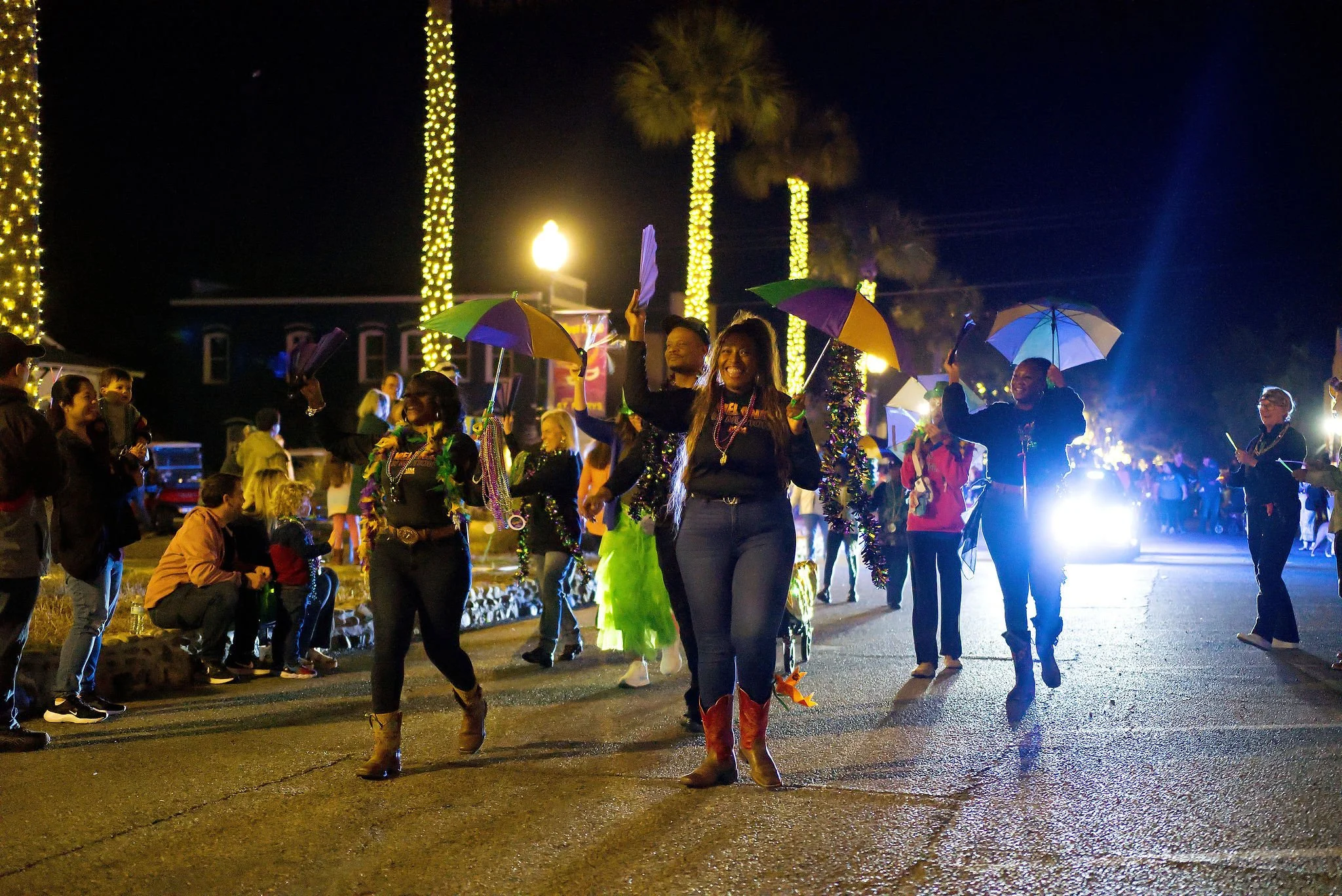 People celebrating at a nighttime parade with Christmas decorations, wearing festive attire and holding umbrellas.