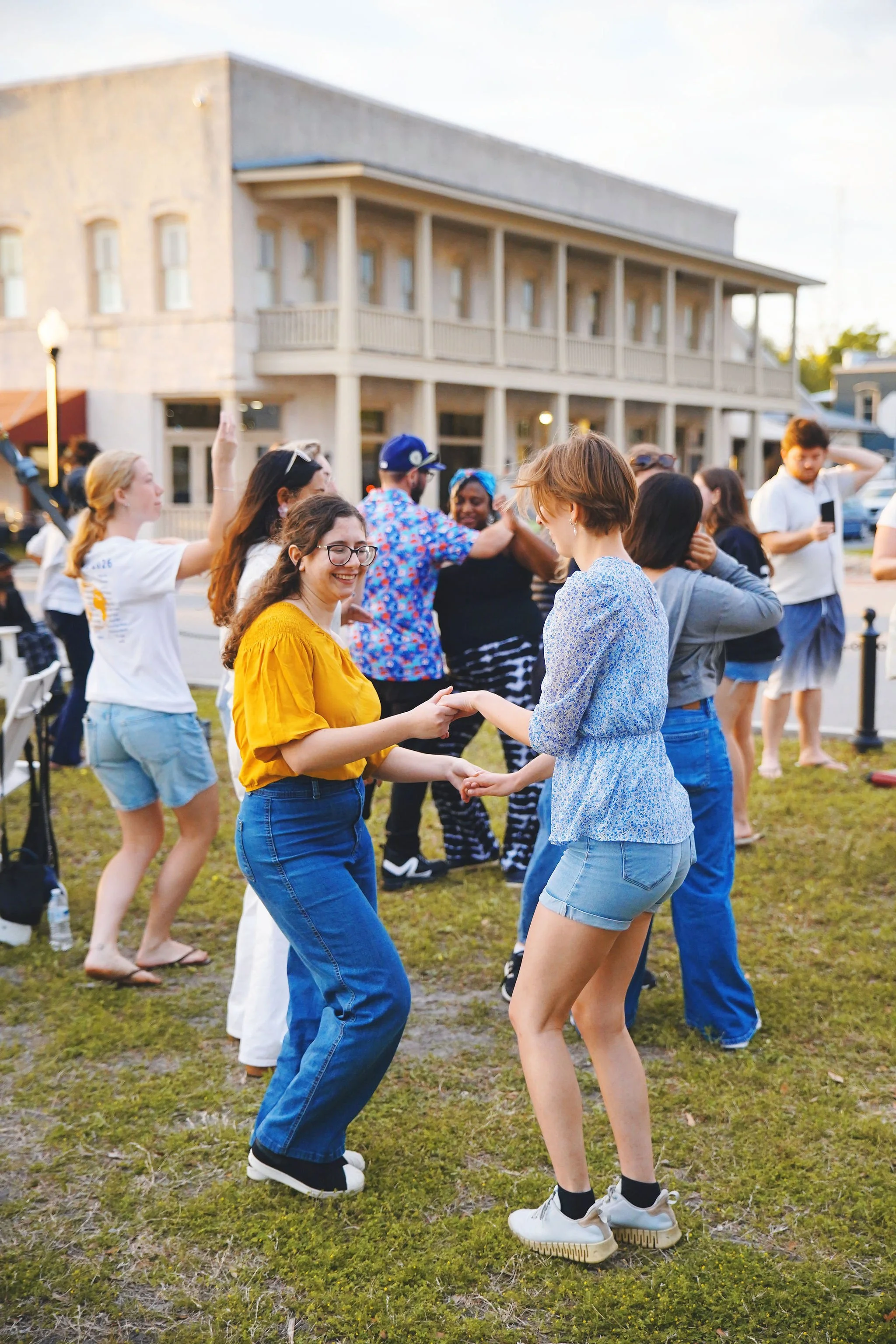 People dancing and socializing outdoors in front of a large building during daylight.