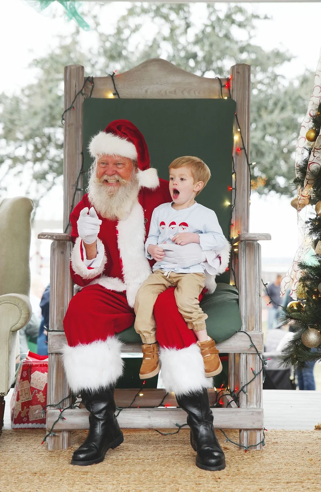 Santa Claus sitting on a throne with a young boy on his lap, in a festive Christmas setting.
