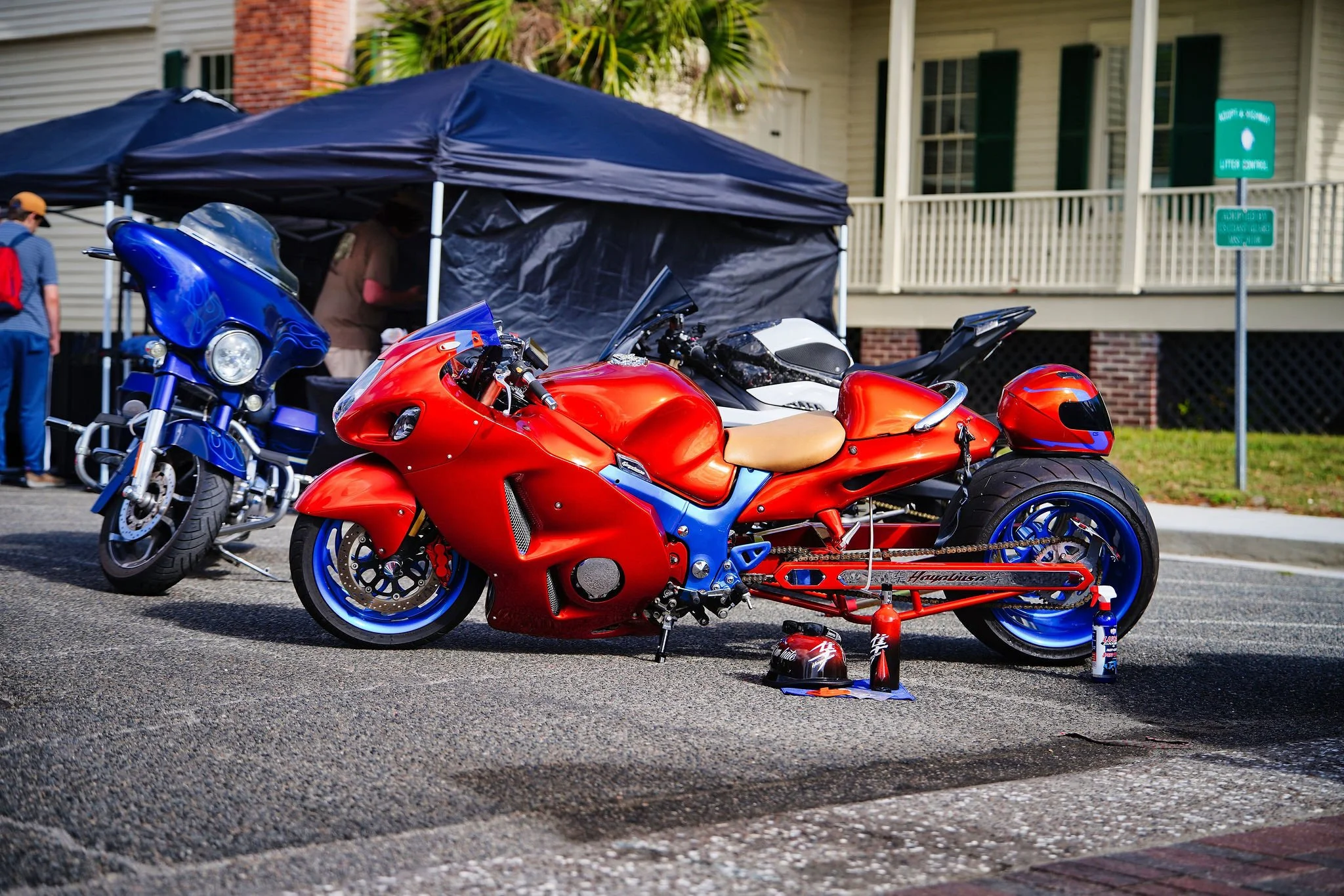 A red sport motorcycle with blue wheels parked next to a blue touring motorcycle, with a tent and people in the background.