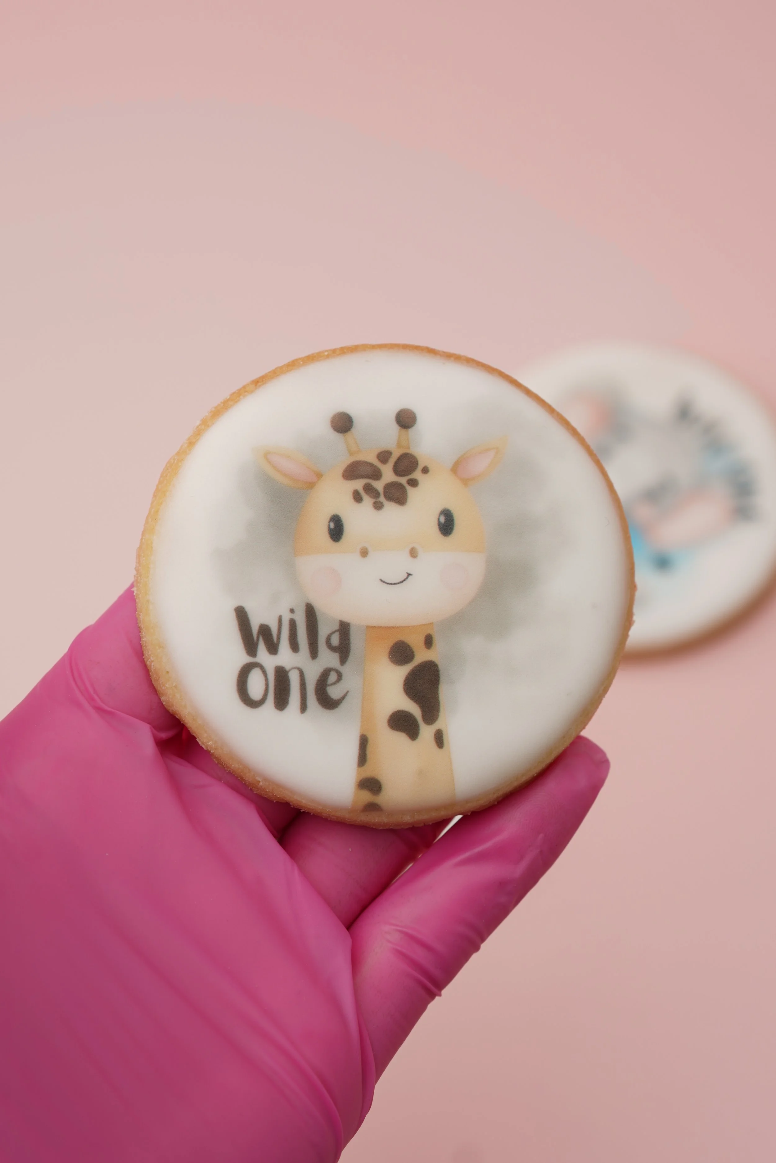 Cookie with a cute giraffe illustration and the words "wild one" on a pink background.