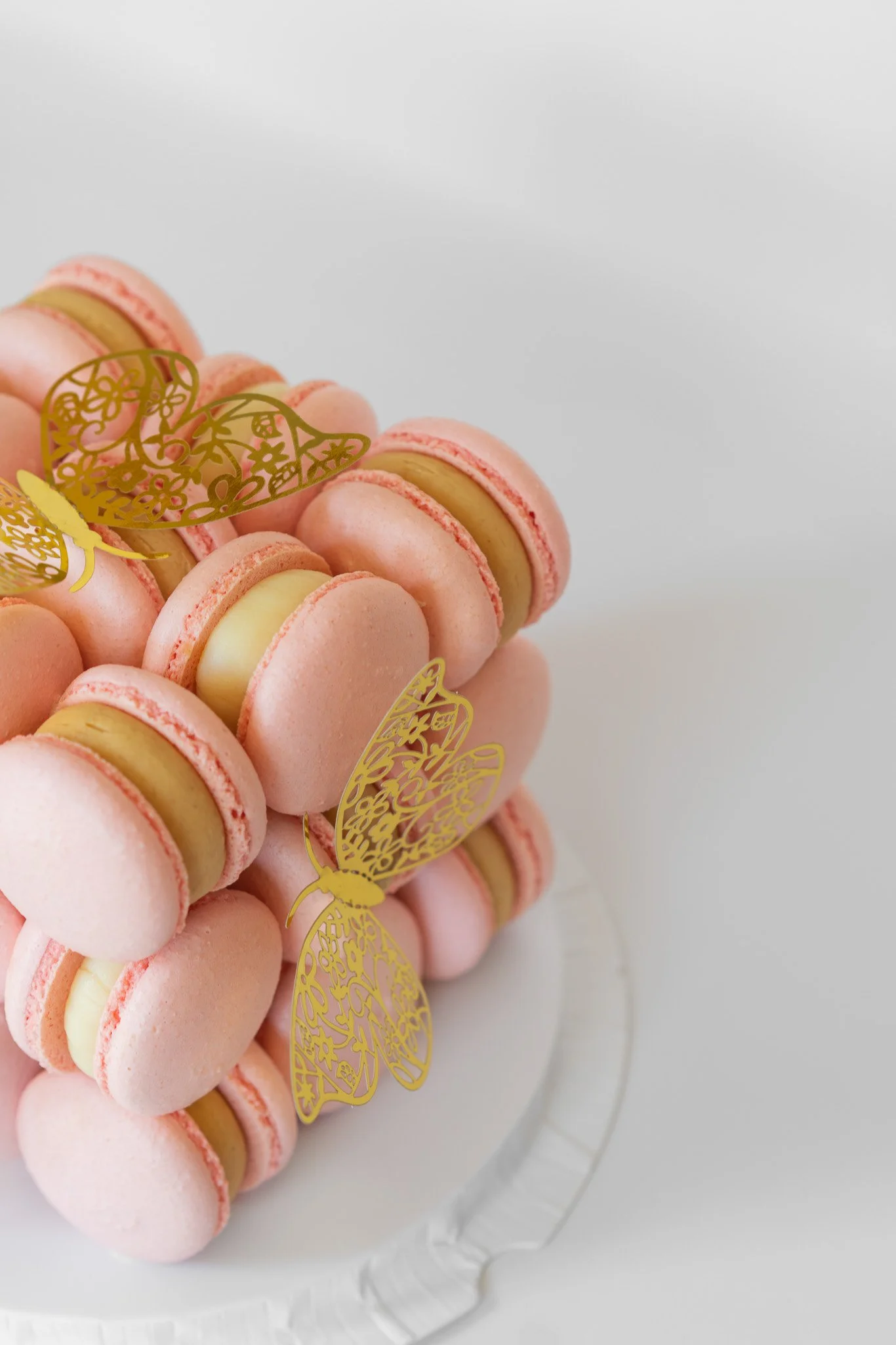 Pink macarons decorated with gold bee and honeycomb shaped toppers on a white cake stand.