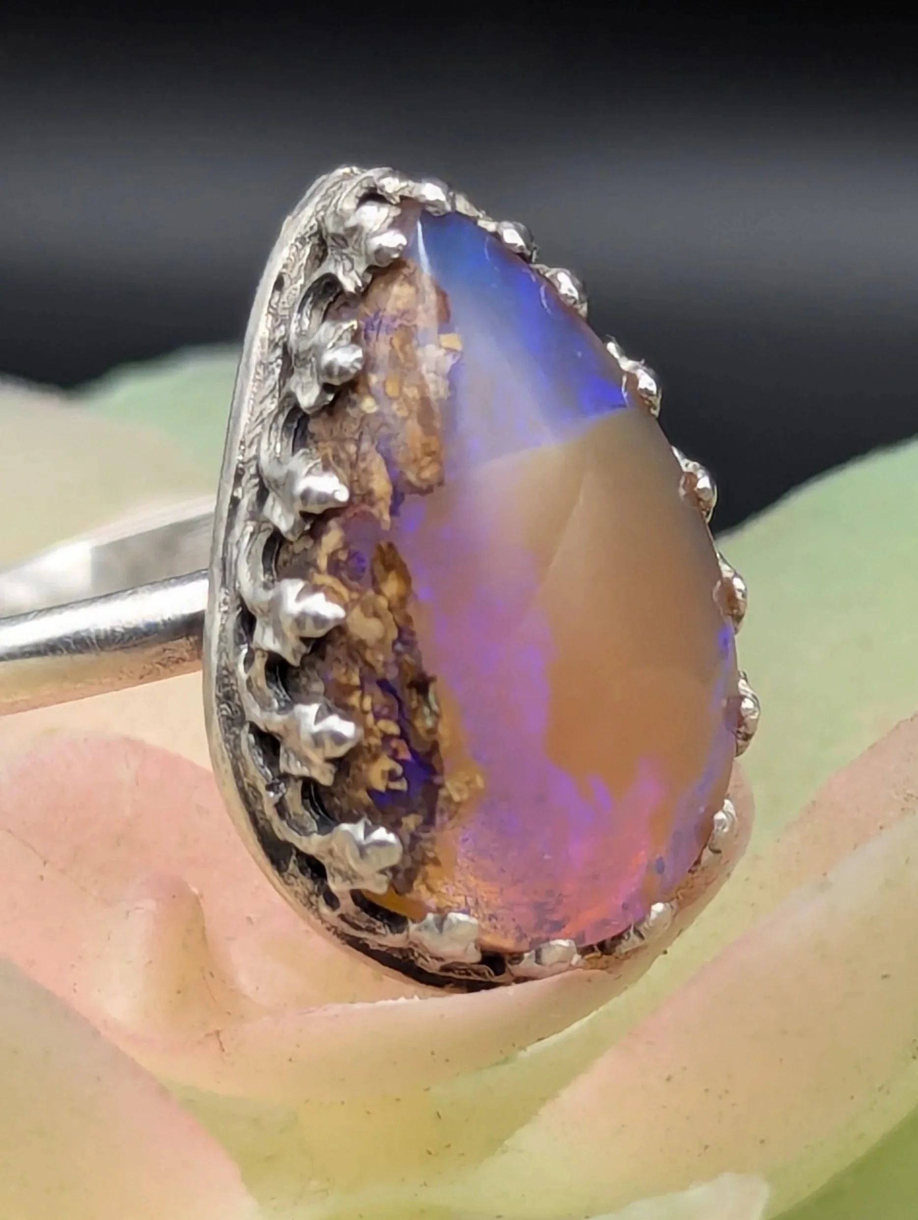Handcrafted sterling silver ring with an pear shaped Australian pipe opal, featuring detailed silverwork. Artisan gemstone jewelry photographed on a multicolored agave.